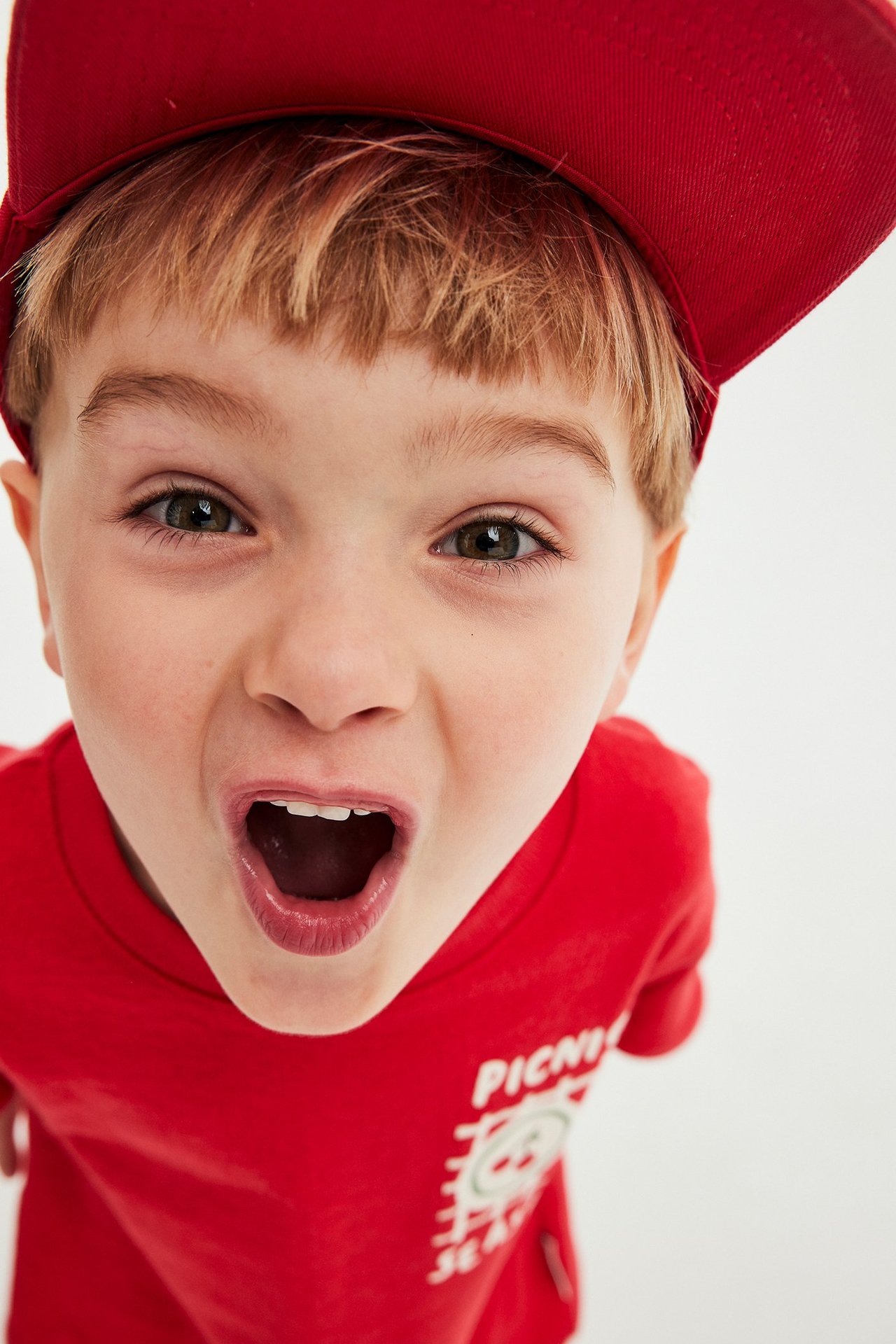 Zbliżenie z przodu na dziecko w czerwonej koszulce z krótkim rękawem z nadrukiem i czerwonej czapce.