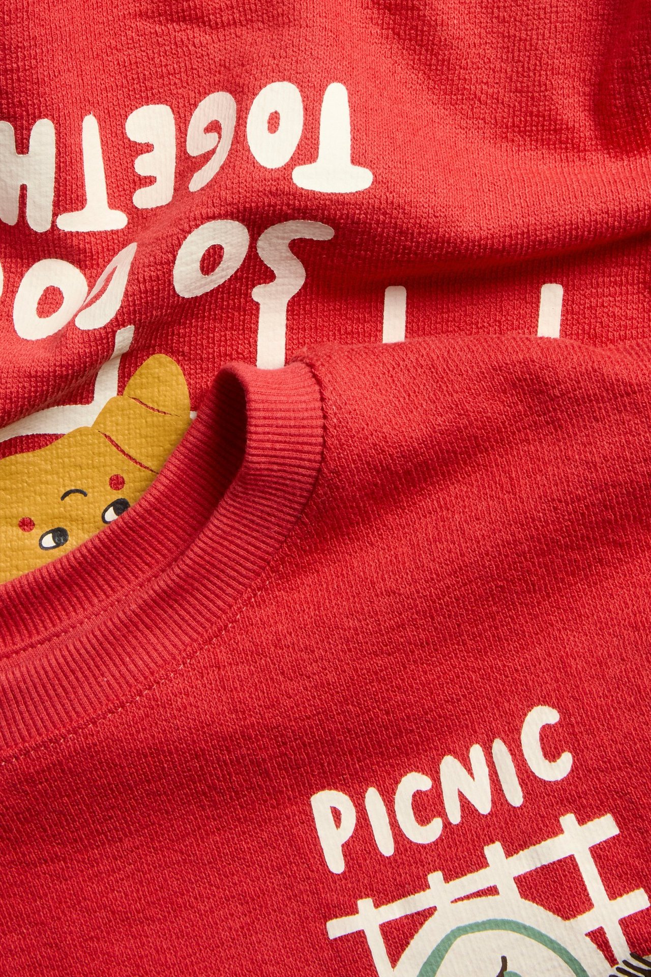 Närbild framifrån av en röd t-shirt i bomull med vit text och ett gult djurtryck.