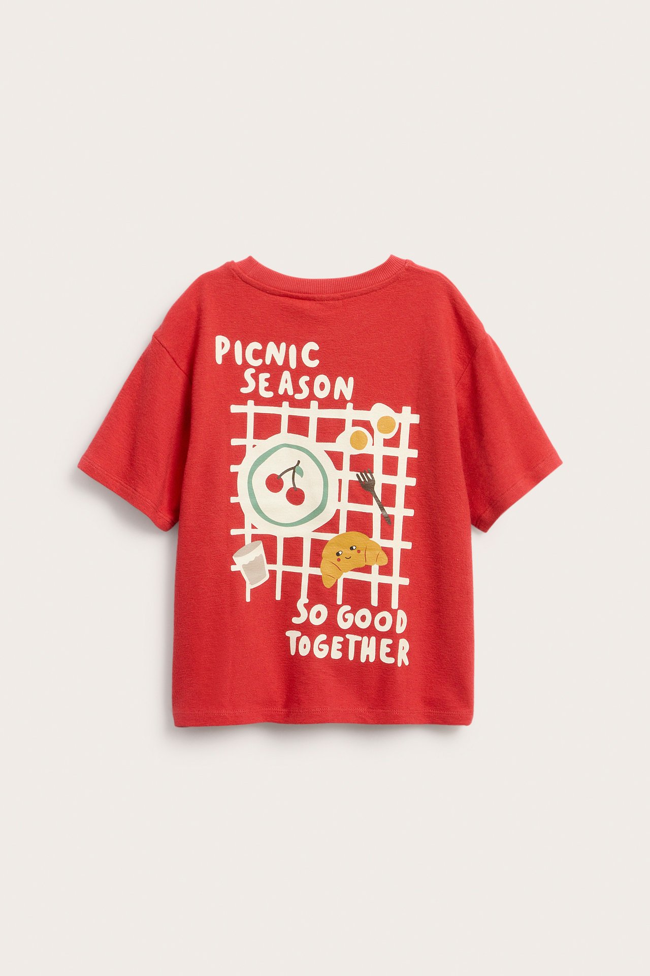 Edestä näkymä lasten punaisesta puuvillaisesta lyhythihaisesta t-paidasta piknik-ruoka- ja tekstipainatuksella.
