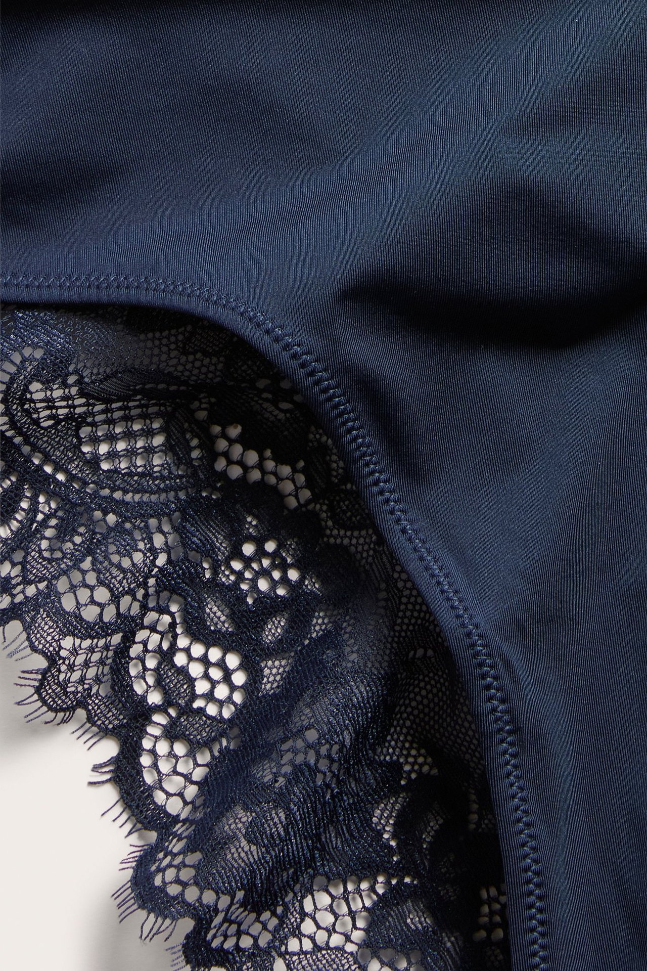 Lähikuva tummansinisistä mikrokangas-alushousuista yksityiskohtaisella pitsikuviolla.