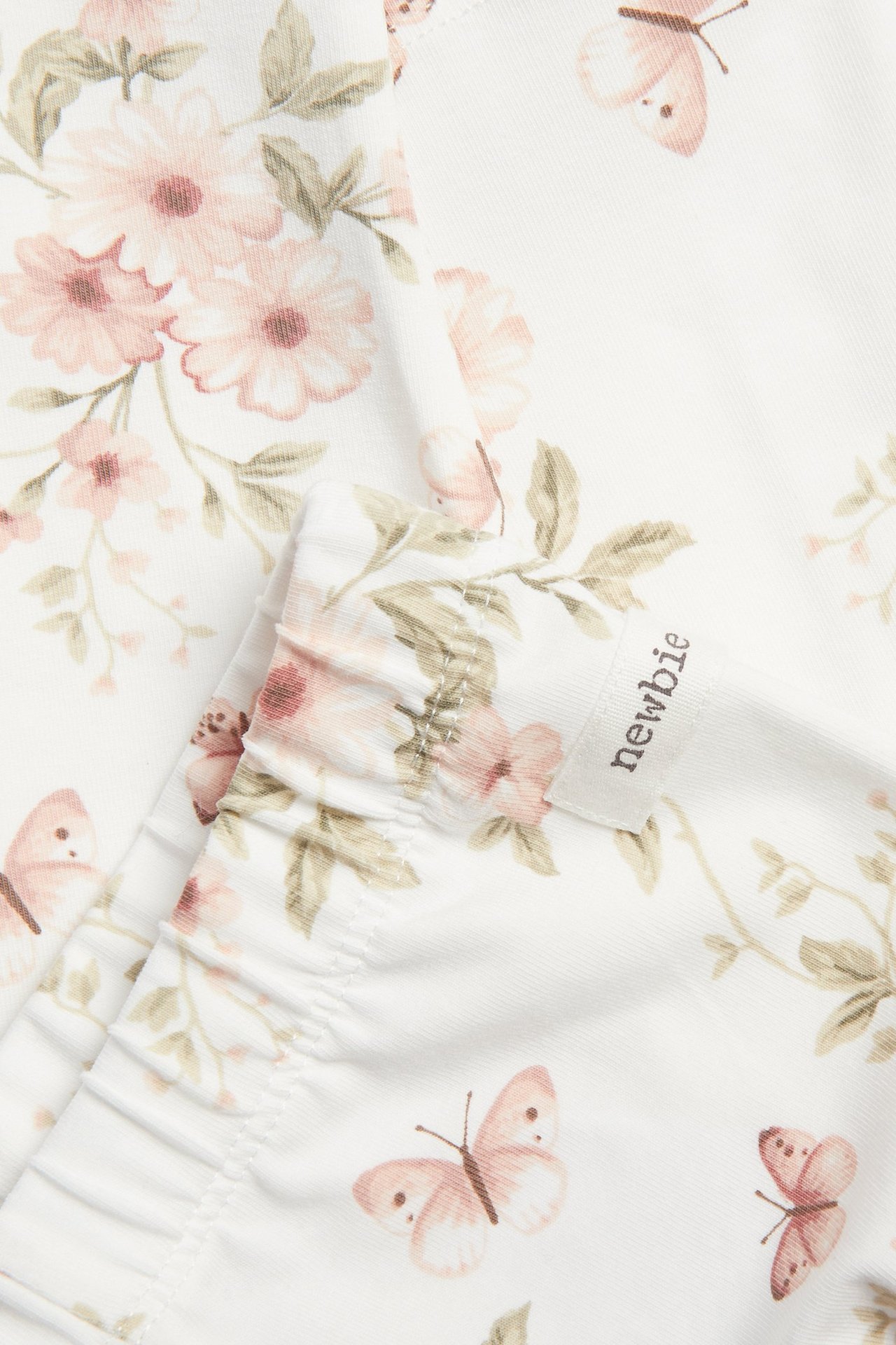 Zbliżenie na off-white legginsy z dżerseju w różowe kwiaty i motyle, elastyczny brzeg.