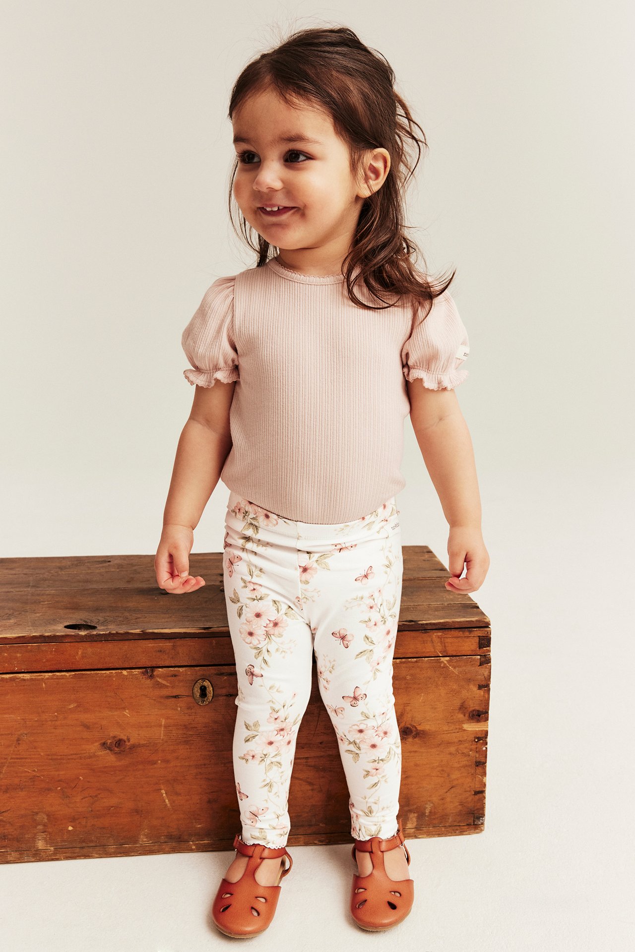 Frontvy av ett barn i offwhite blommiga leggings, ljusrosa ribbad topp och bruna skor.
