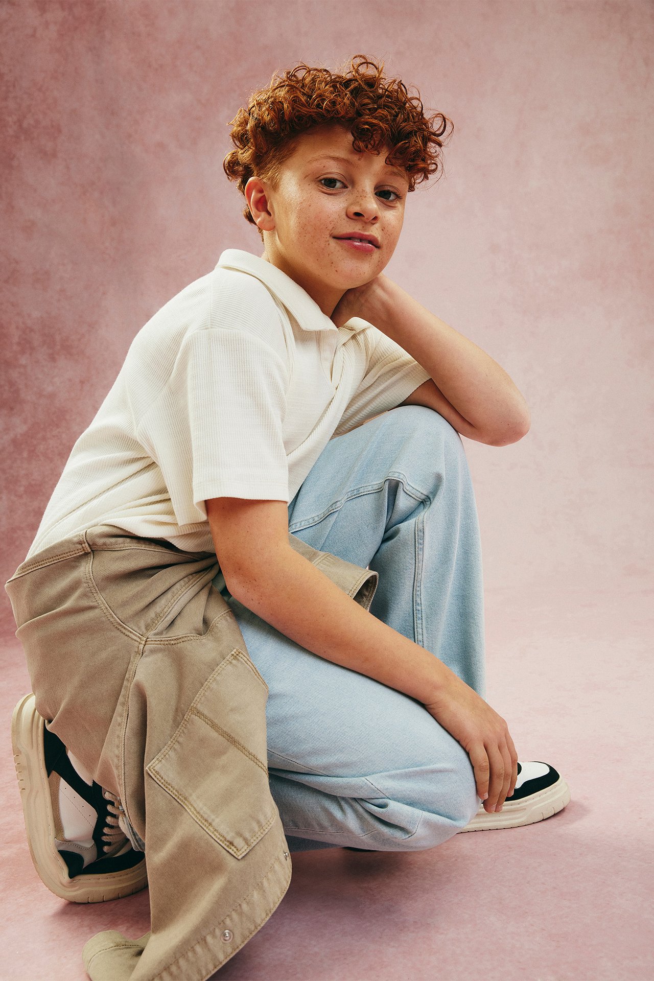 Frontvy på ett barn i offwhite ribbad pikétröja, ljusblå vida jeans och svartvita sneakers.