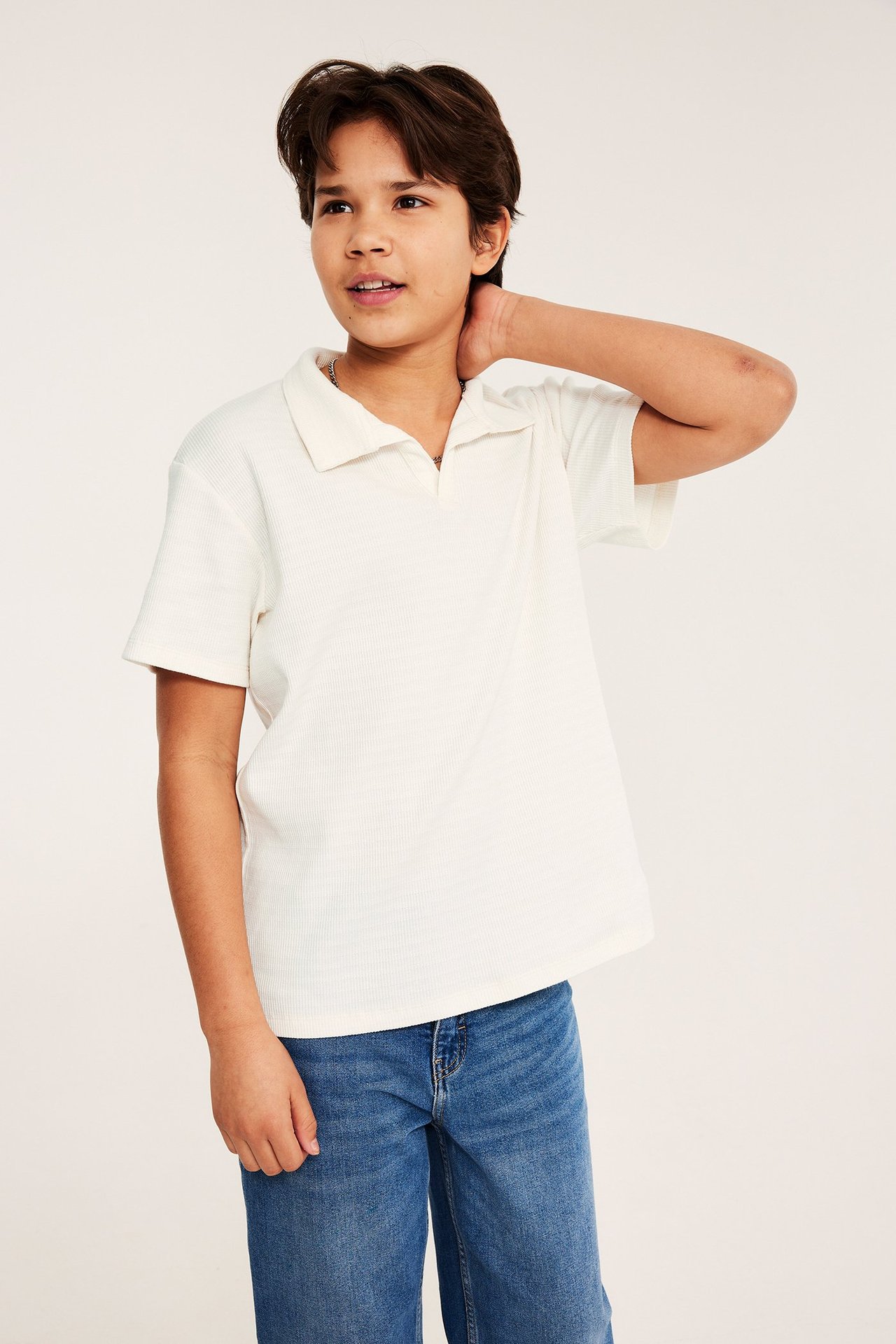Edestäpäin, lapsi yllään luonnonvalkoinen lyhythihainen teksturoitu pikeepaita ja siniset farkut.