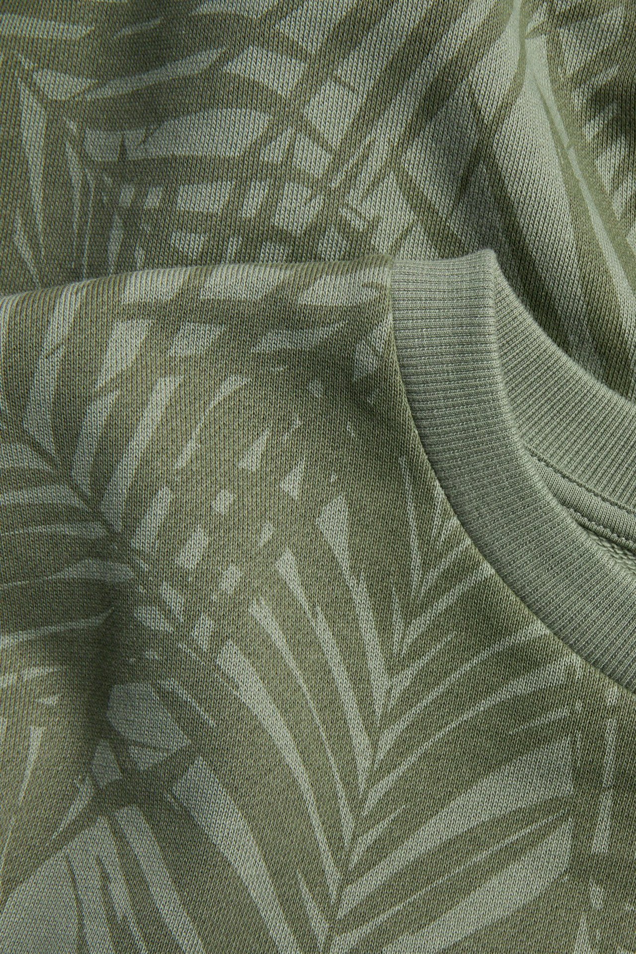 Lähikuva vihreästä kuvioidusta froteehupparista, jossa ribbineulottu pyöreä pääntie ja palmunlehtiprintti.