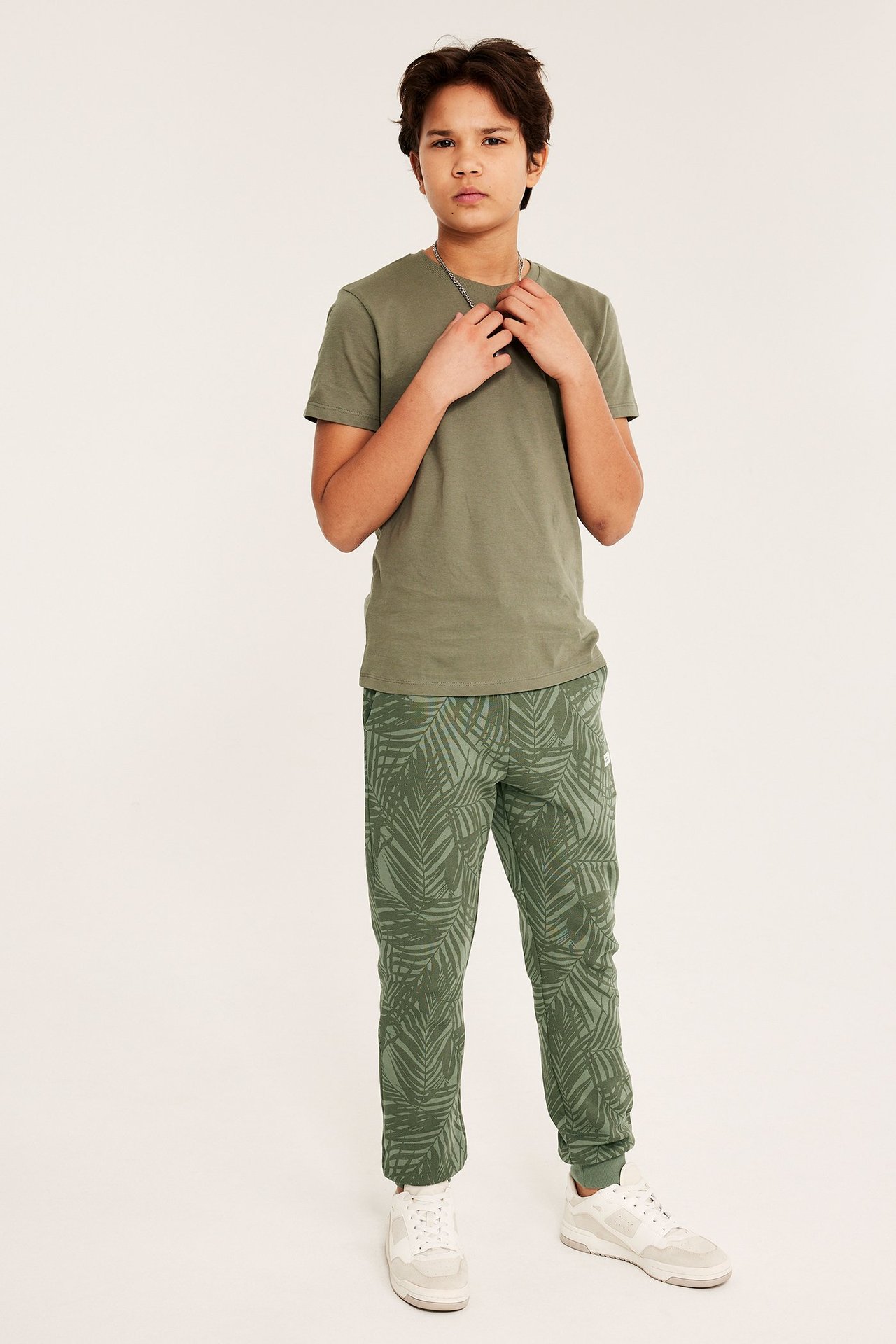 Widok z przodu: dziecko w zielonych wzorzystych dresach, oliwkowym t-shircie i białych trampkach.