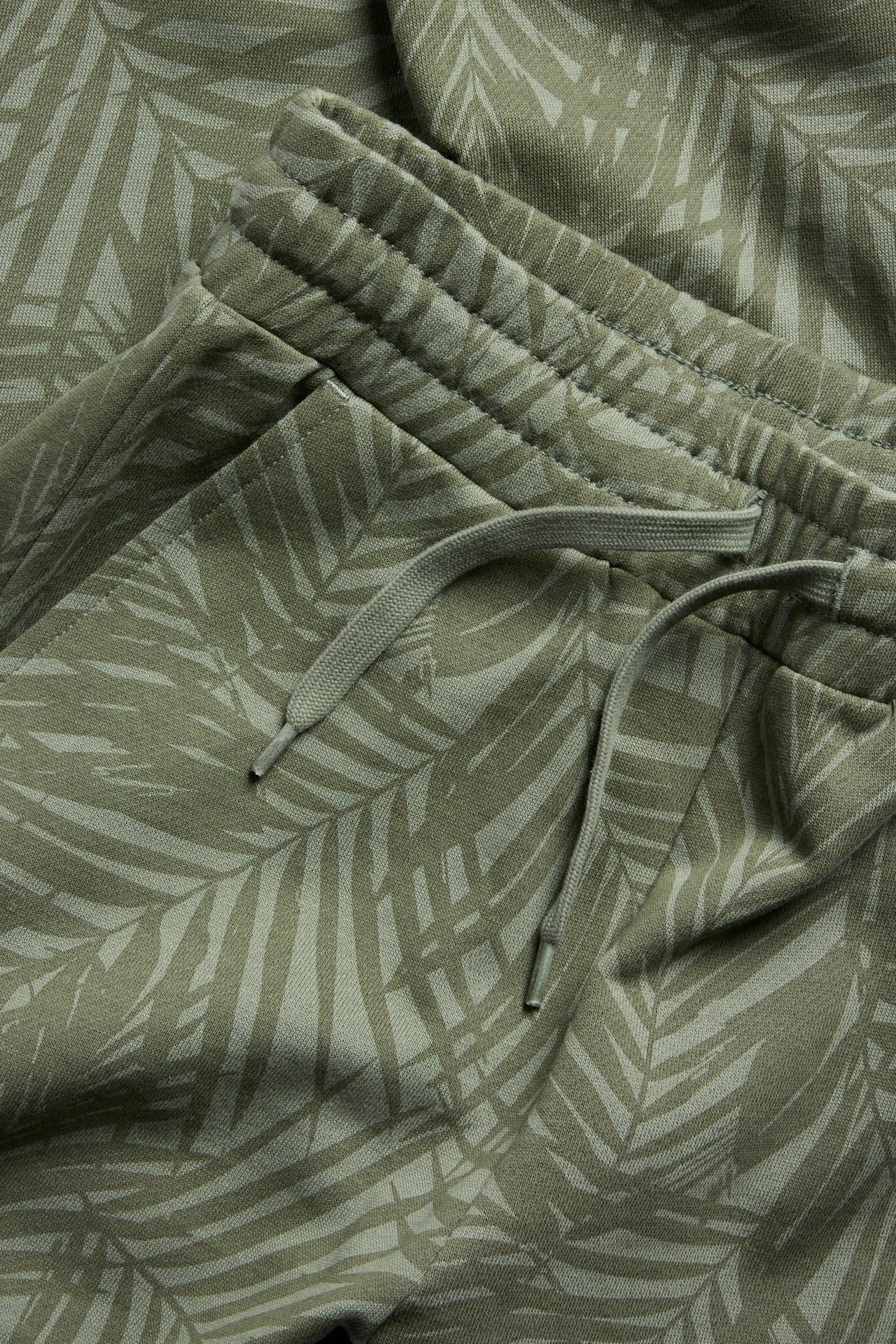 Lähikuva vihreistä kuvioiduista puuvillaverkkareista, joissa on palmunlehtiprintti, joustava kiristysnyöri vyötäröllä ja taskut.