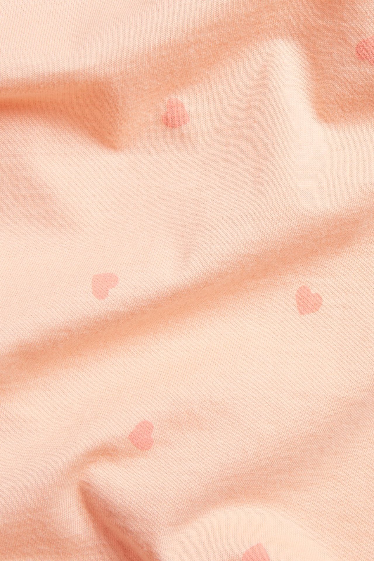 Zbliżenie na jasno pomarańczowy bawełniany top z dzianiny z wzorem w małe serca.