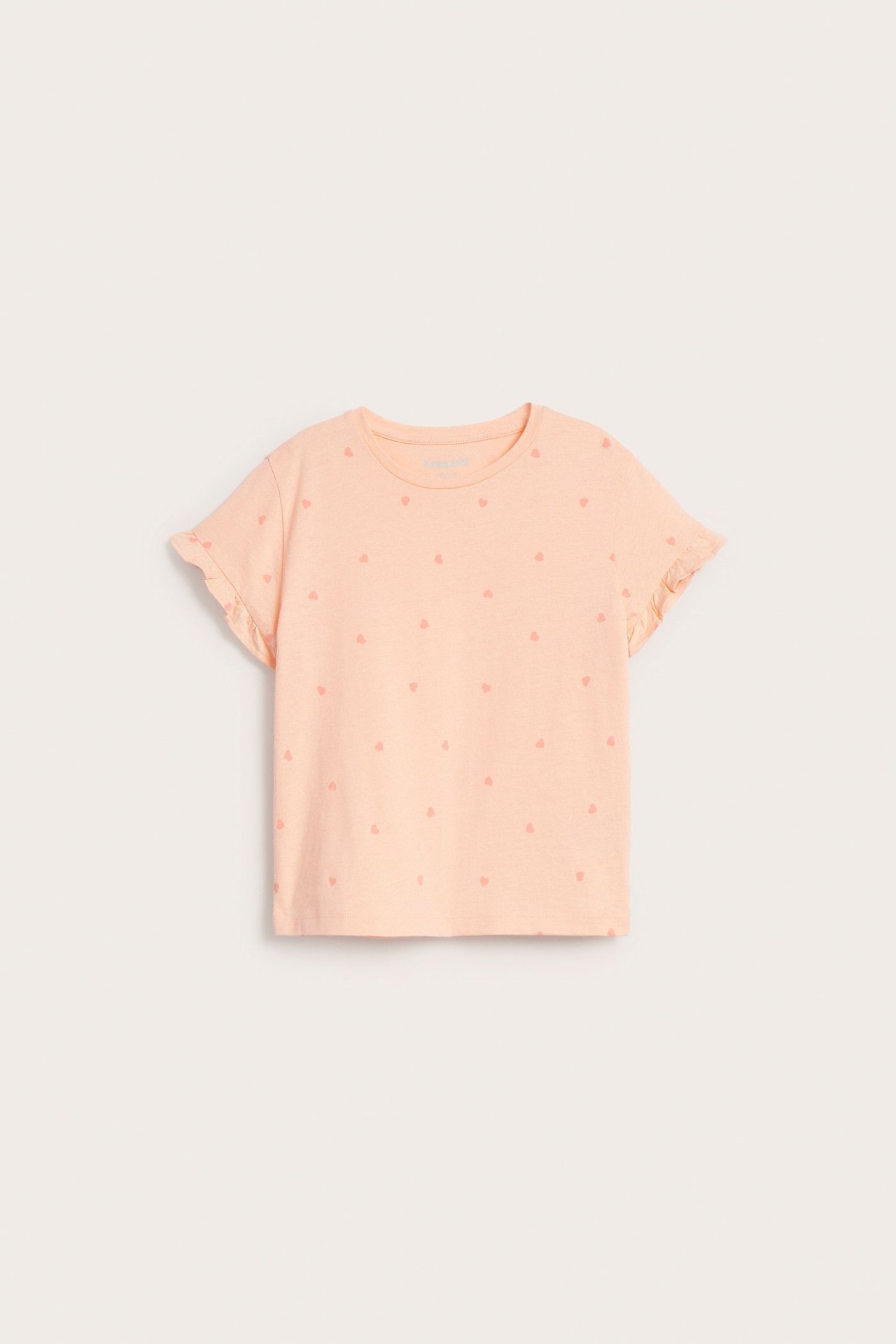 Framsida på en barntröja i ljus orange bomull med hjärtmönster, lös passform och volangärmar.