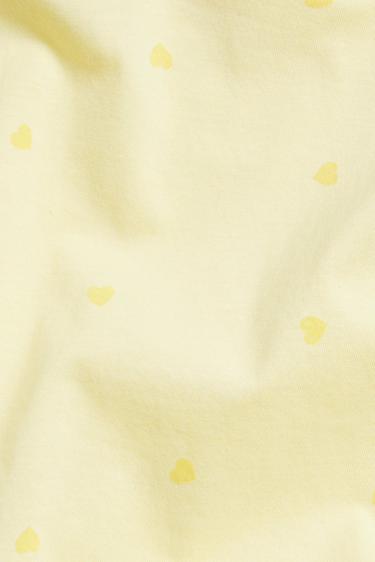 Lähikuva vaaleankeltaisesta puuvillaneuloksesta, jossa on pieniä sydänkuvioita.