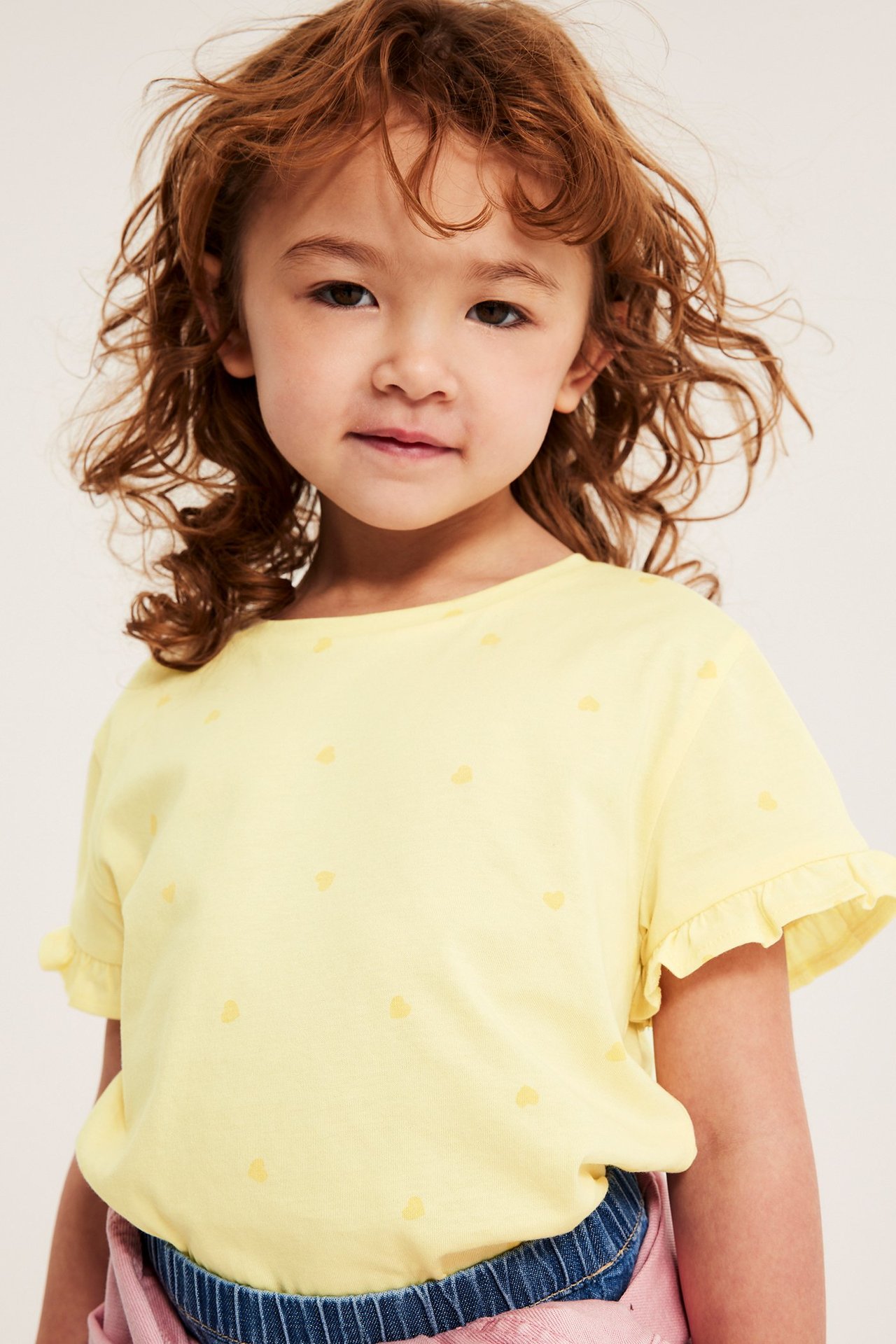 Närbild framifrån på ett barn i ljusgul bomullstopp med hjärtmönster och volangärmar.