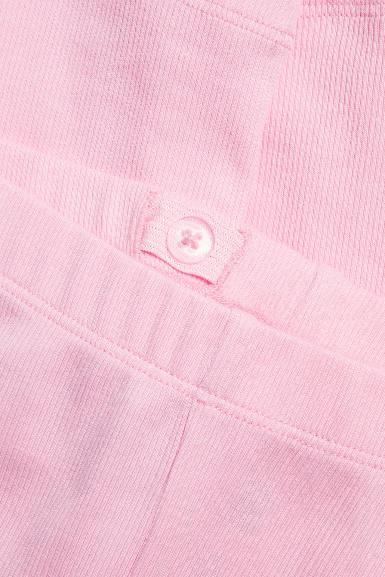 Zbliżenie na różowe, prążkowane legginsy dla dzieci z regulowanym pasem na guzik.