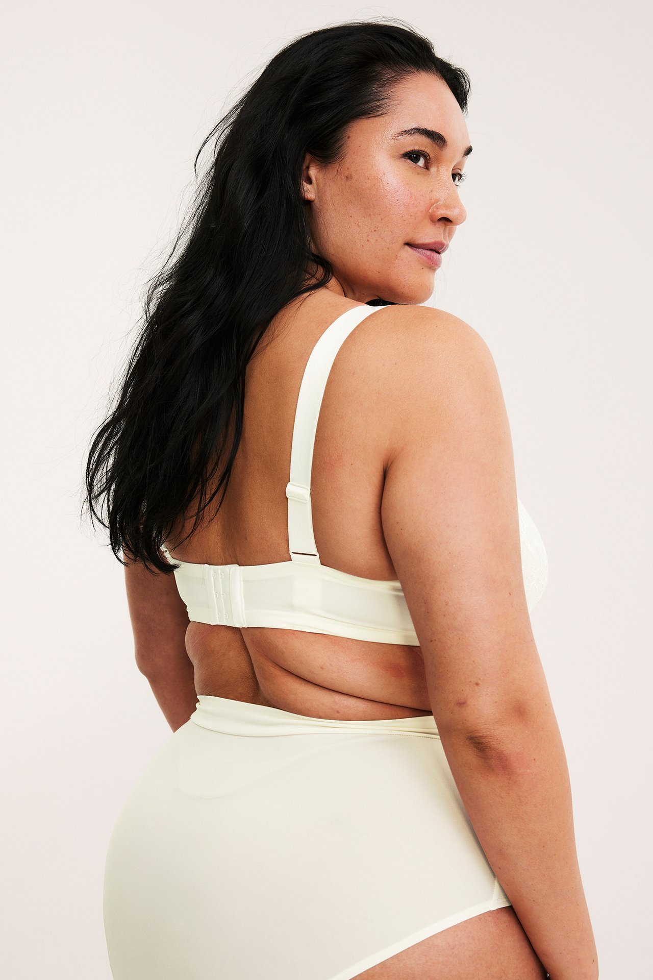 Naisen takakuva luonnonvalkoisissa korkeavyötäröisissä muotoilevissa alushousuissa ja yhteensopivissa rintaliiveissä.