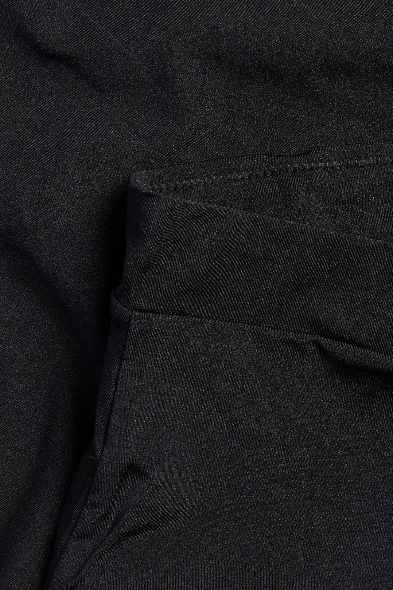 Lähikuva mustista korkeavyötäröisistä alushousuista, joissa on kevyt muotoilu, hohtava pinta ja joustava vyötärö.