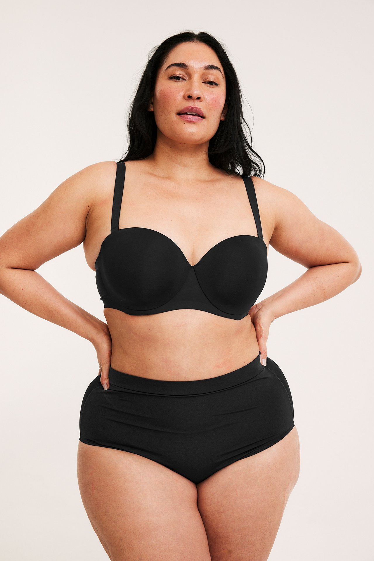 Edestä: nainen mustissa korkeavyötäröisissä muotoilevissa pikkuhousuissa ja mustissa rintaliiveissä.