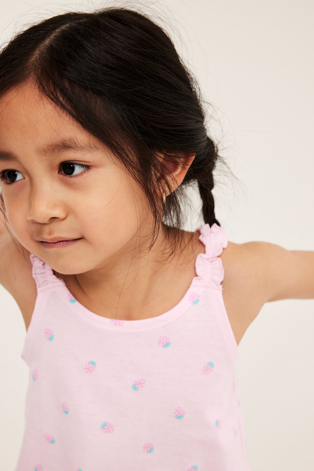 Nærbilde, forfra: Barn i rosa bomullspyjamatopp med jordbærtrykk og volangstropper.