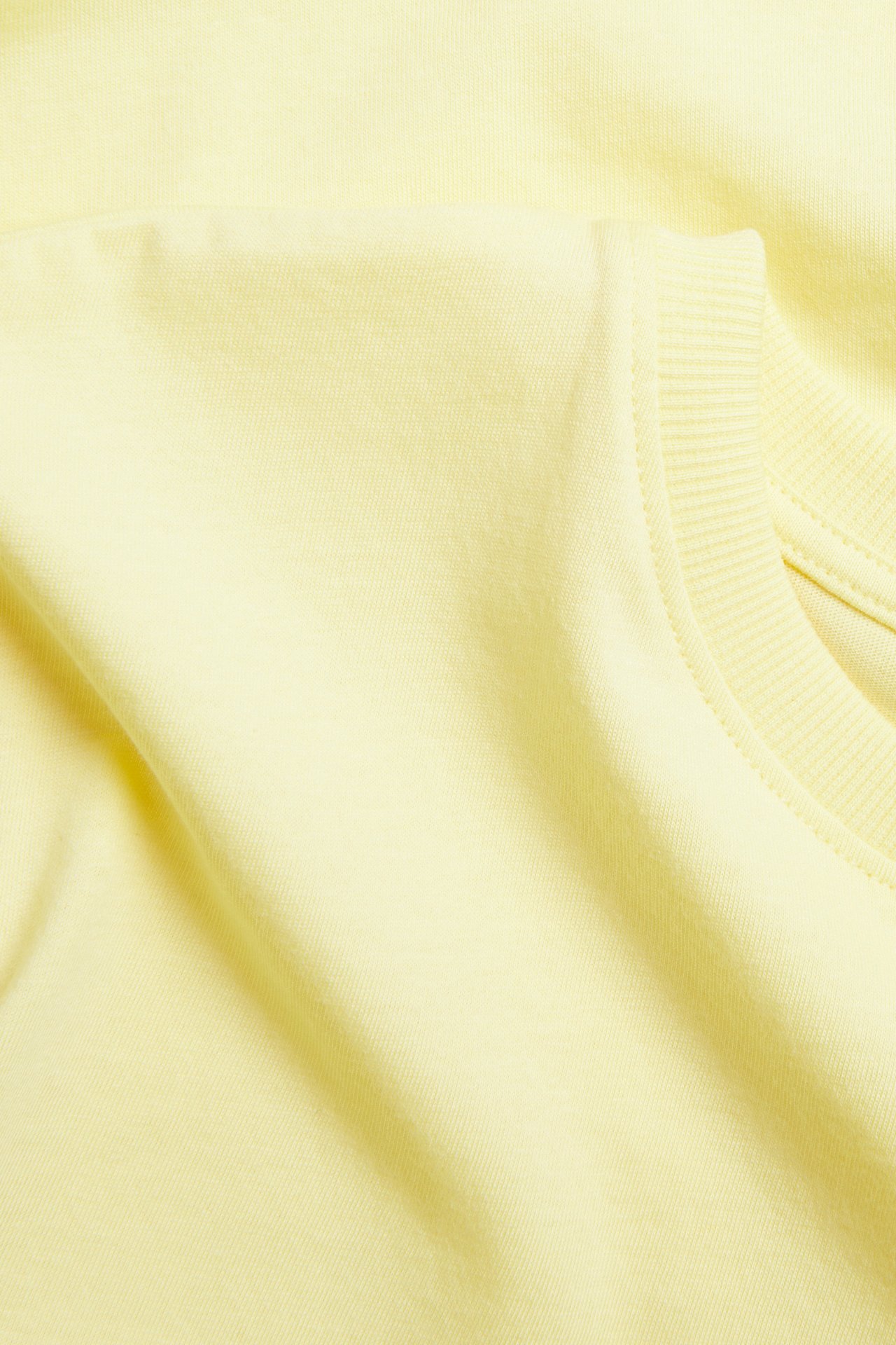 Lähikuva yksivärisestä vaaleankeltaisesta puuvillaisesta lyhythihaisesta t-paidasta resoripääntieellä.