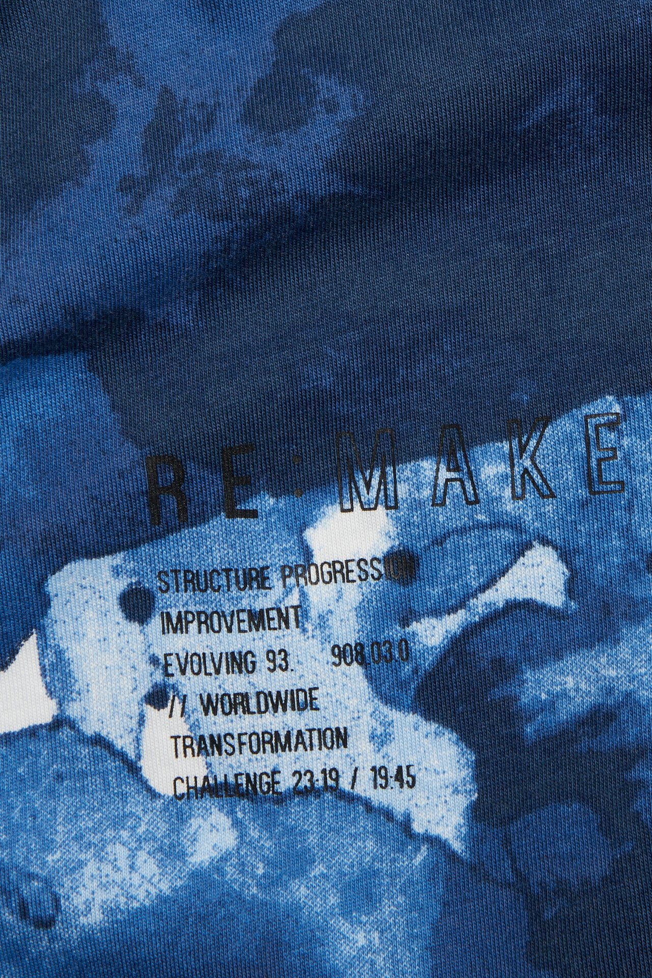 Lähikuva edestä lapsen oversized puuvillaisesta t-paidasta sinivalkoisella abstraktilla kuviolla ja mustalla tekstipainatuksella.