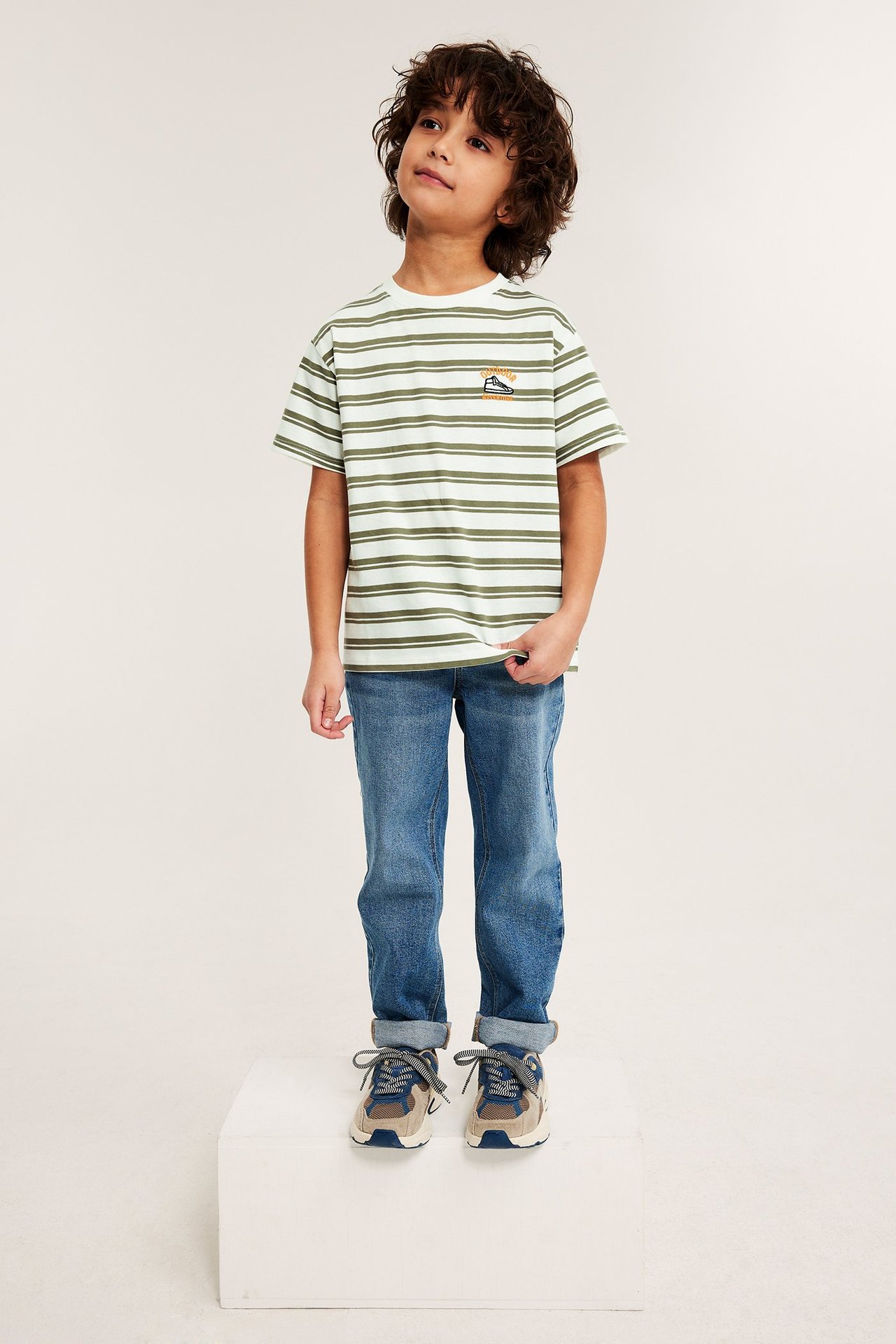 Front view: Lapsi yllään offwhite, vihreäraidallinen oversized t-paita, siniset farkut ja tennarit.