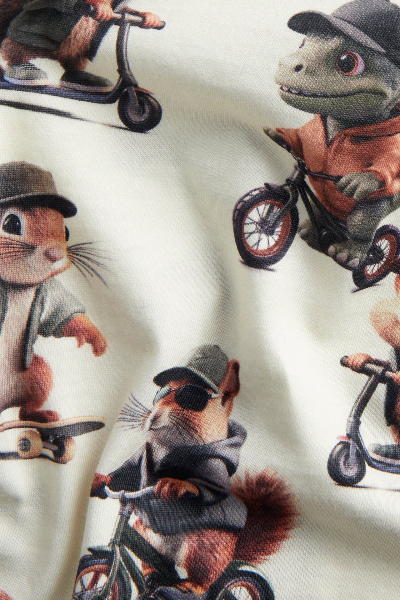 Närbild av en benvit t-shirt i bomull för barn, med djurmönster på cyklar och skateboards.