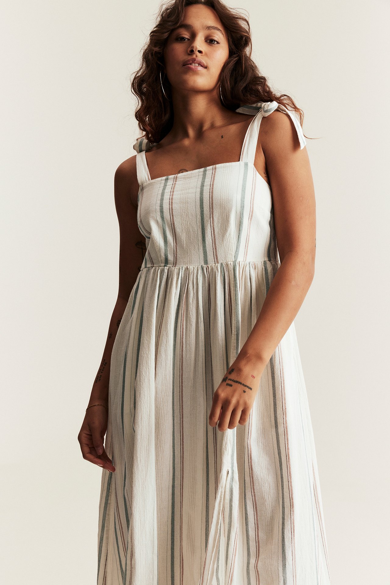 Kobieta, widok z przodu: kremowa sukienka w paski z bawełny, wiązane ramiączka, marszczony tył.