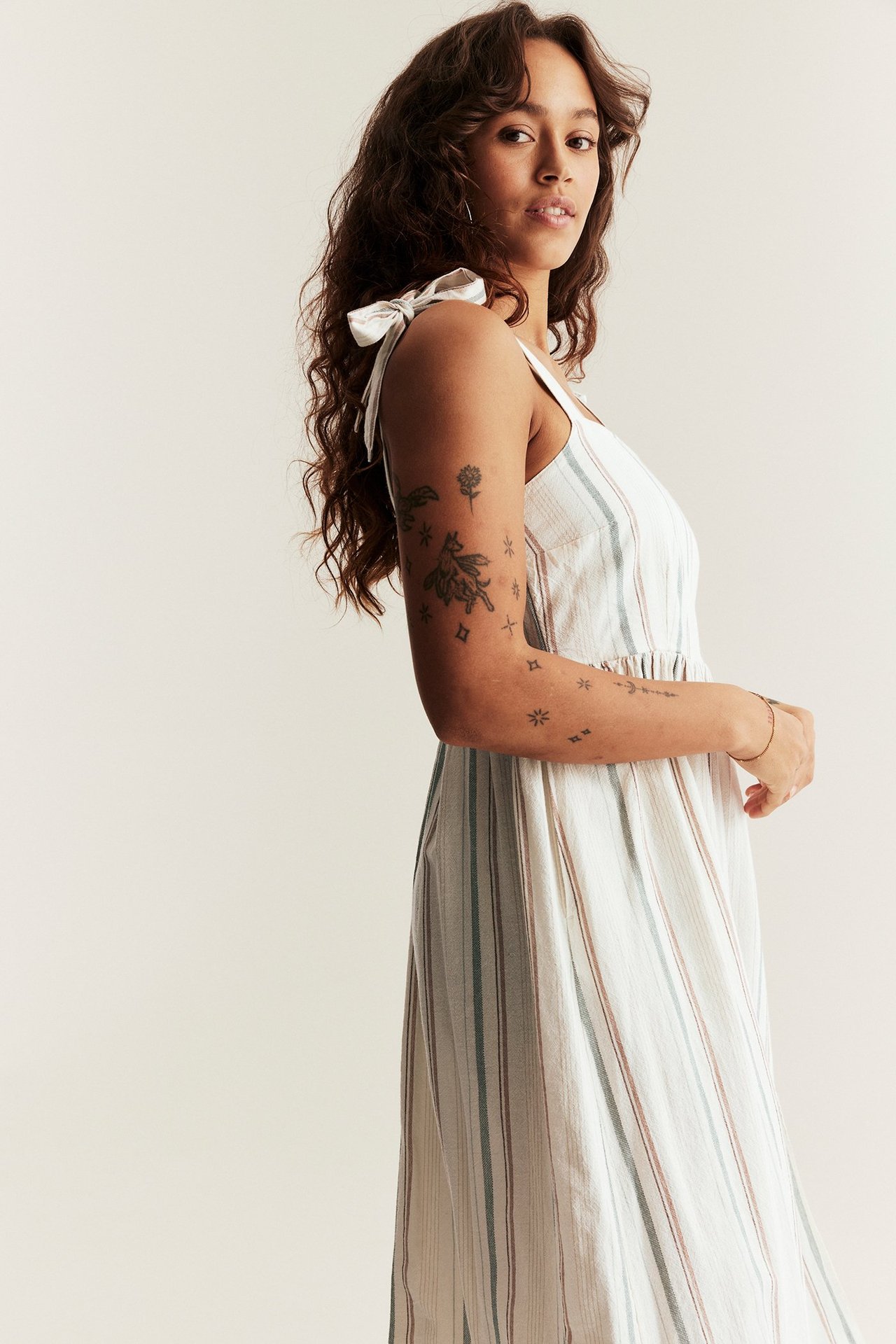 Widok z boku kobiety w biało-paskowej bawełnianej sukience z wiązanymi ramiączkami i marszczoną talią.