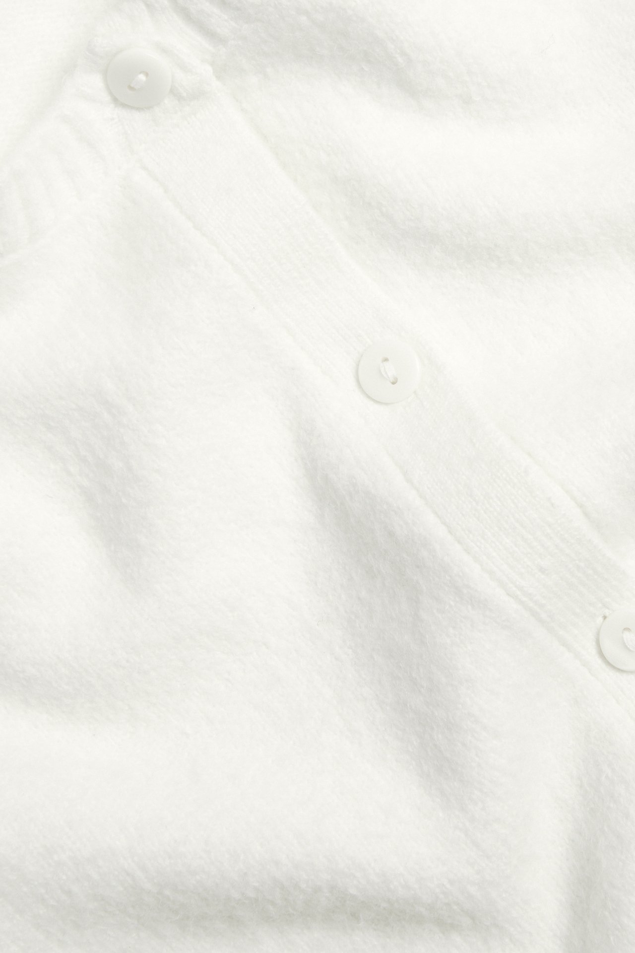 Närbild av en offwhite stickad kortärmscardigan med synliga knappar.