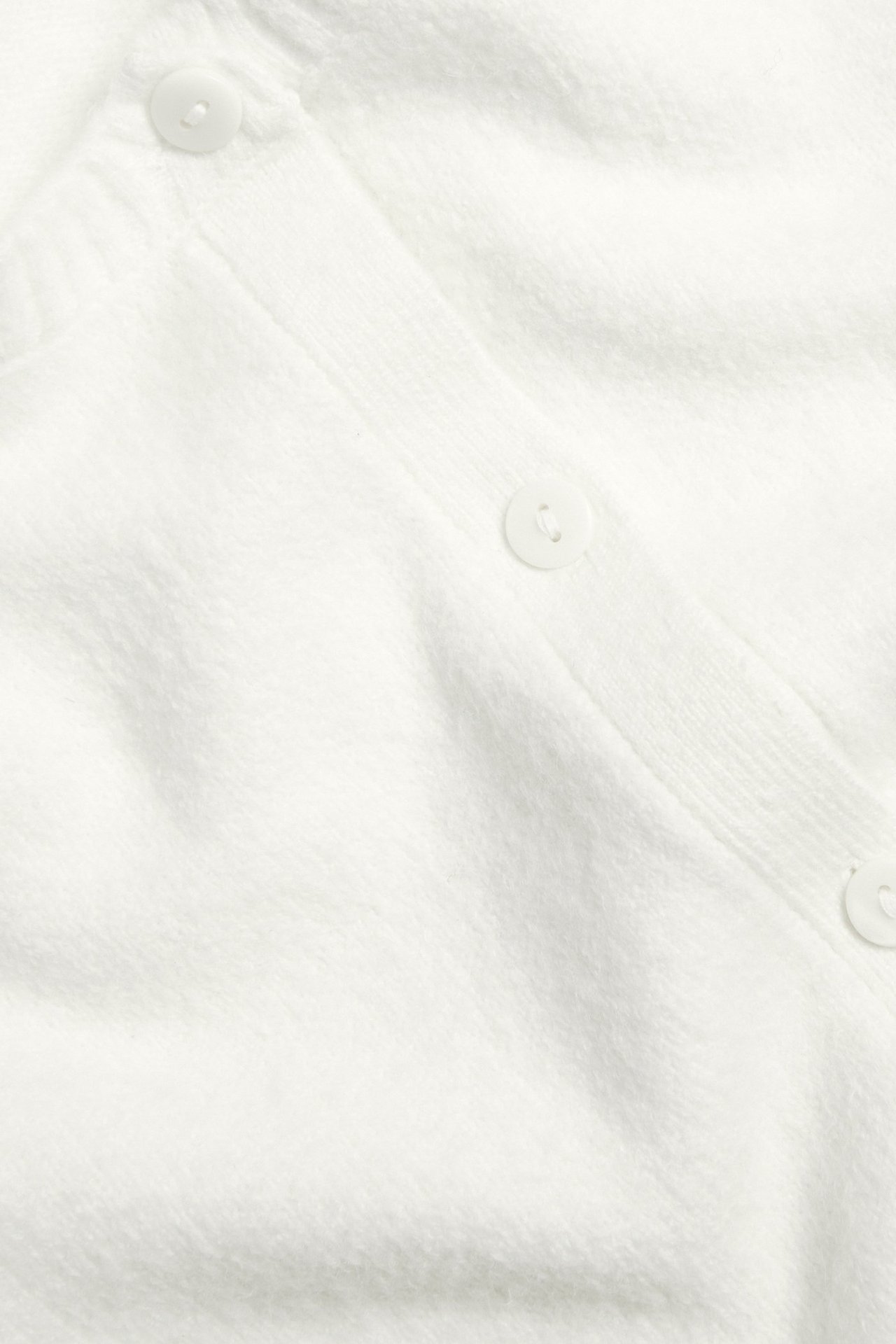 Zbliżenie na kremowy dzianinowy kardigan z krótkim rękawem, z widocznymi guzikami z przodu.