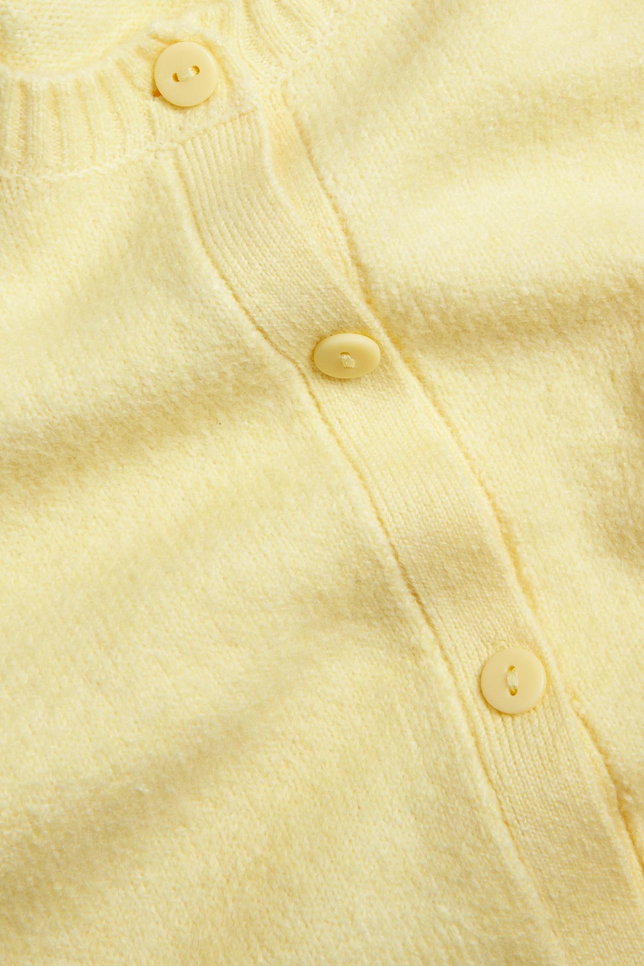 Närbild framifrån på en ljusgul stickad kortärmad kofta med matchande knappar.