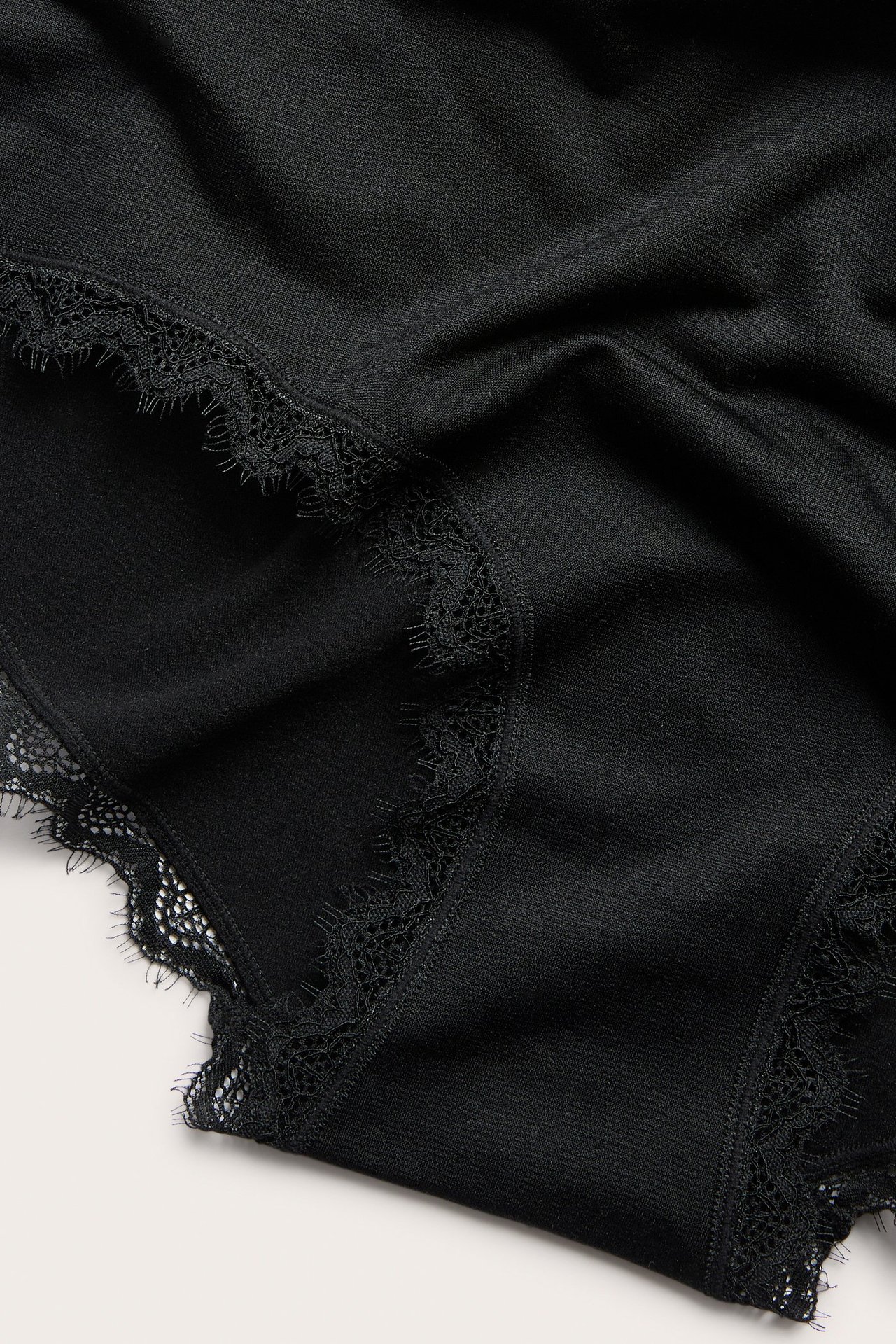 Lähikuva mustista yksivärisistä pitsikoristelluista hipster-alushousuista, polyamidia ja elastaania.