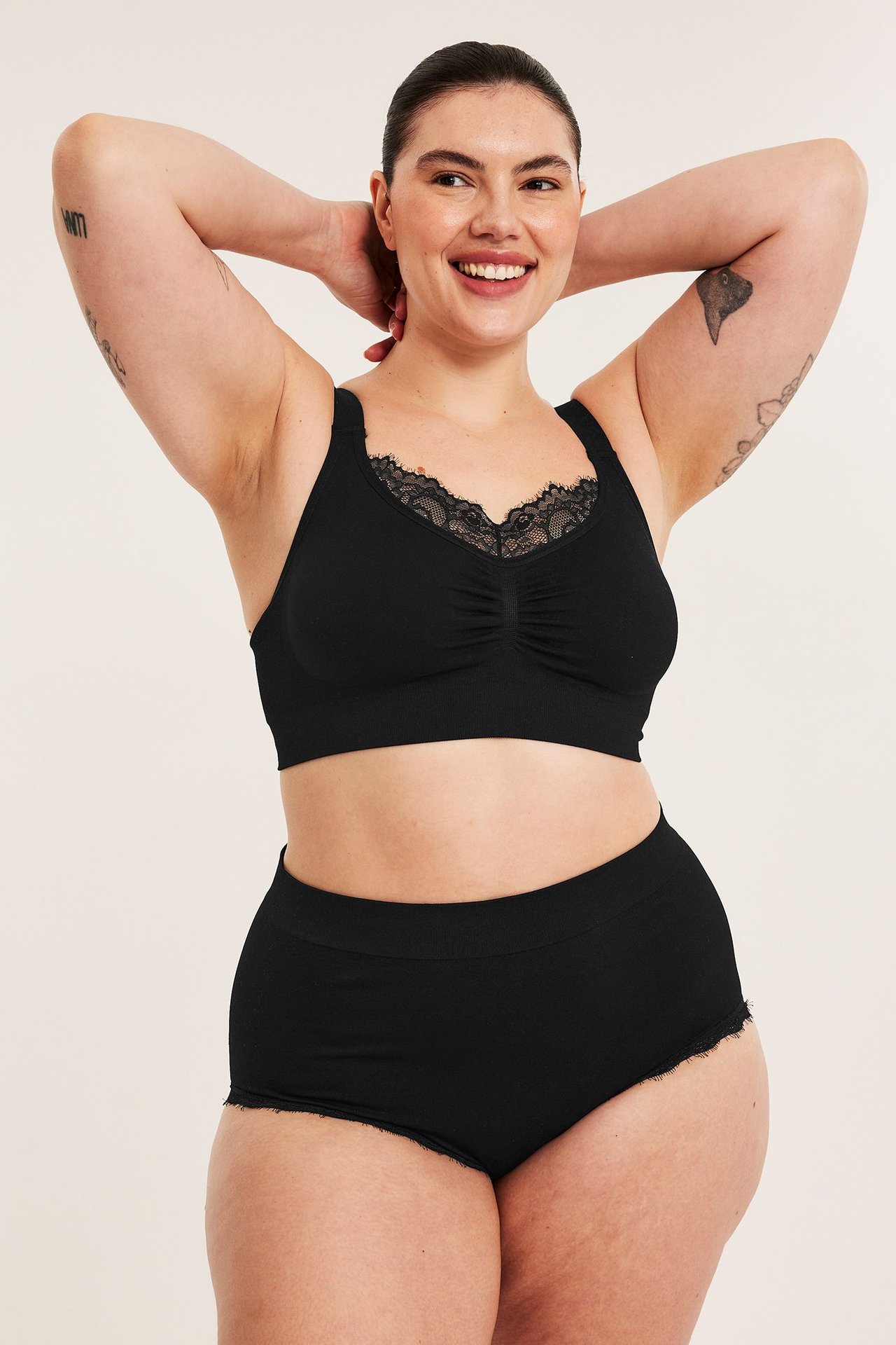 Frontbilde av kvinne i svart sømløs hipster-truse og matchende svart bralette med blondekant.