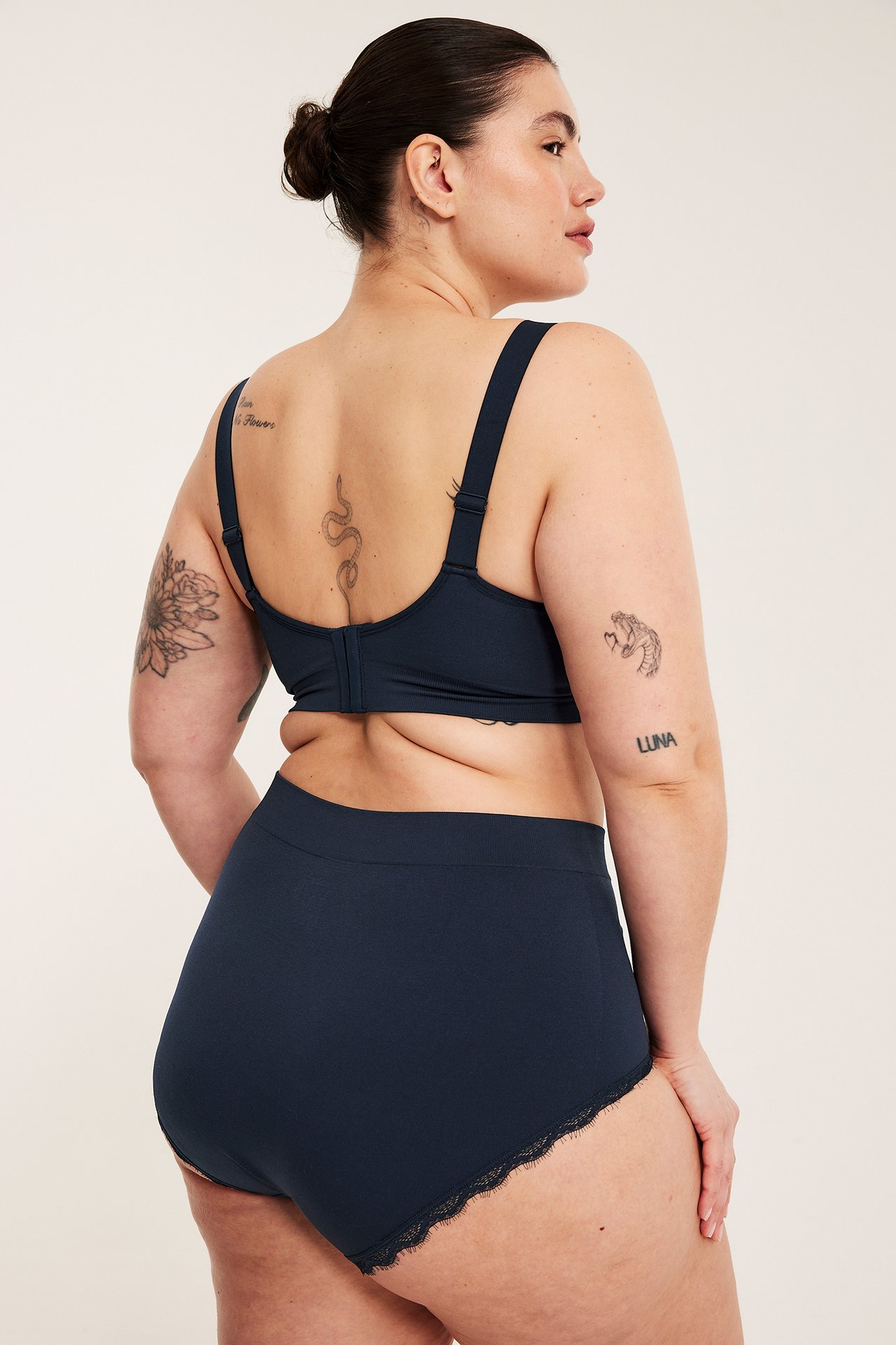 Bakifrån kvinna i mörkblå enfärgade hipstertrosor med spets och matchande behå.