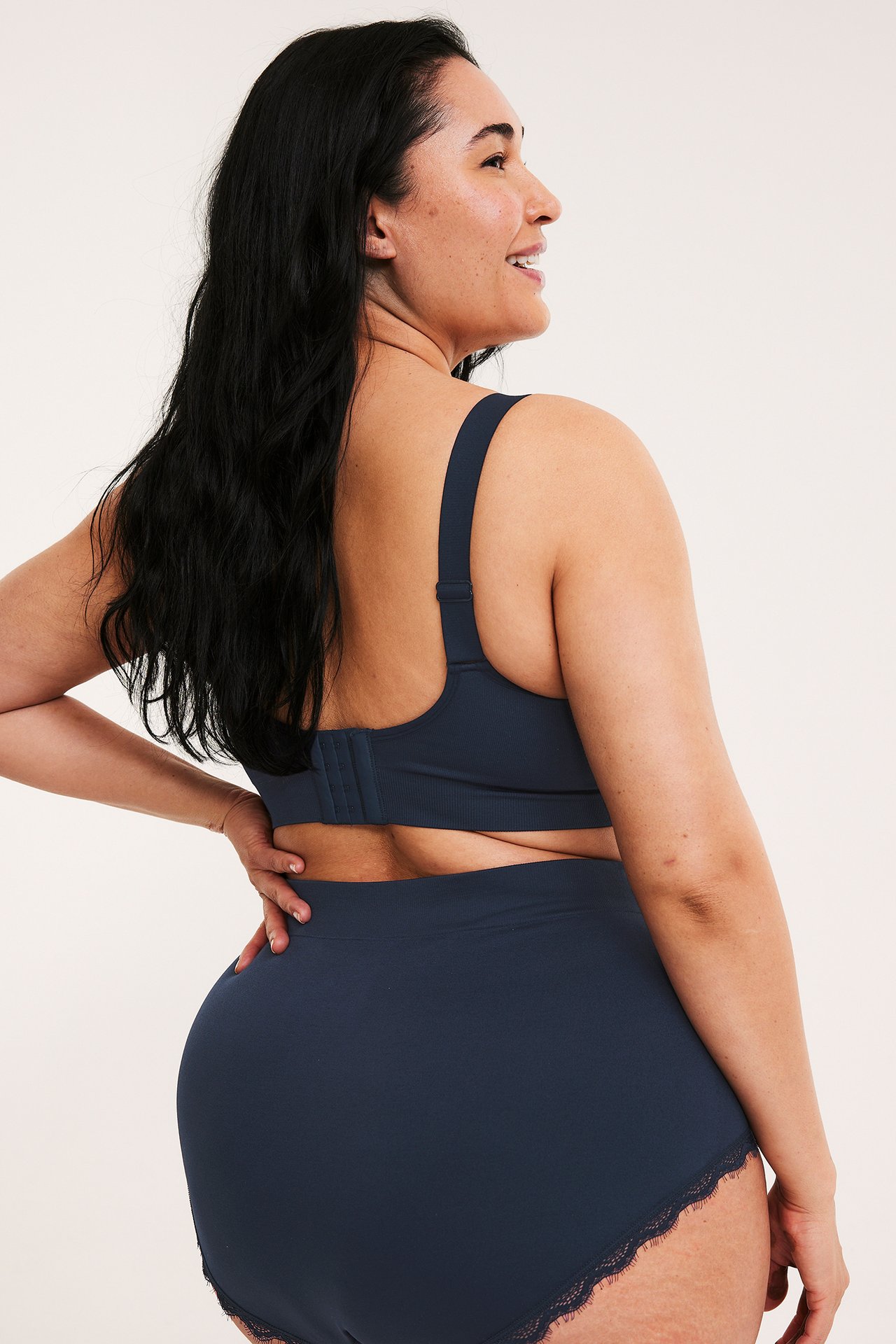 Bakifrån kvinna i mörkblå sömlösa höga hipster trosor med spets och matchande behå.