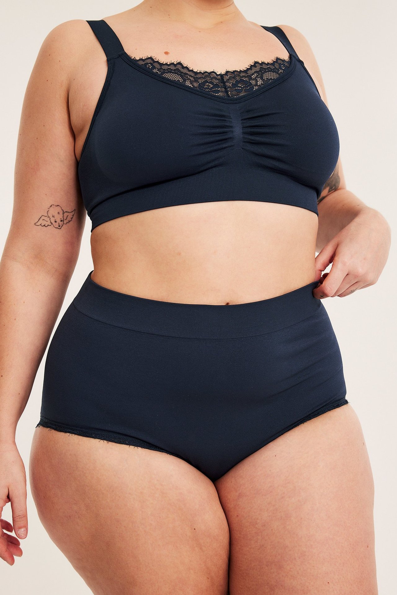 Framifrån, kvinna i mörkblå sömlösa hipstertrosor och matchande spetskantad BH.