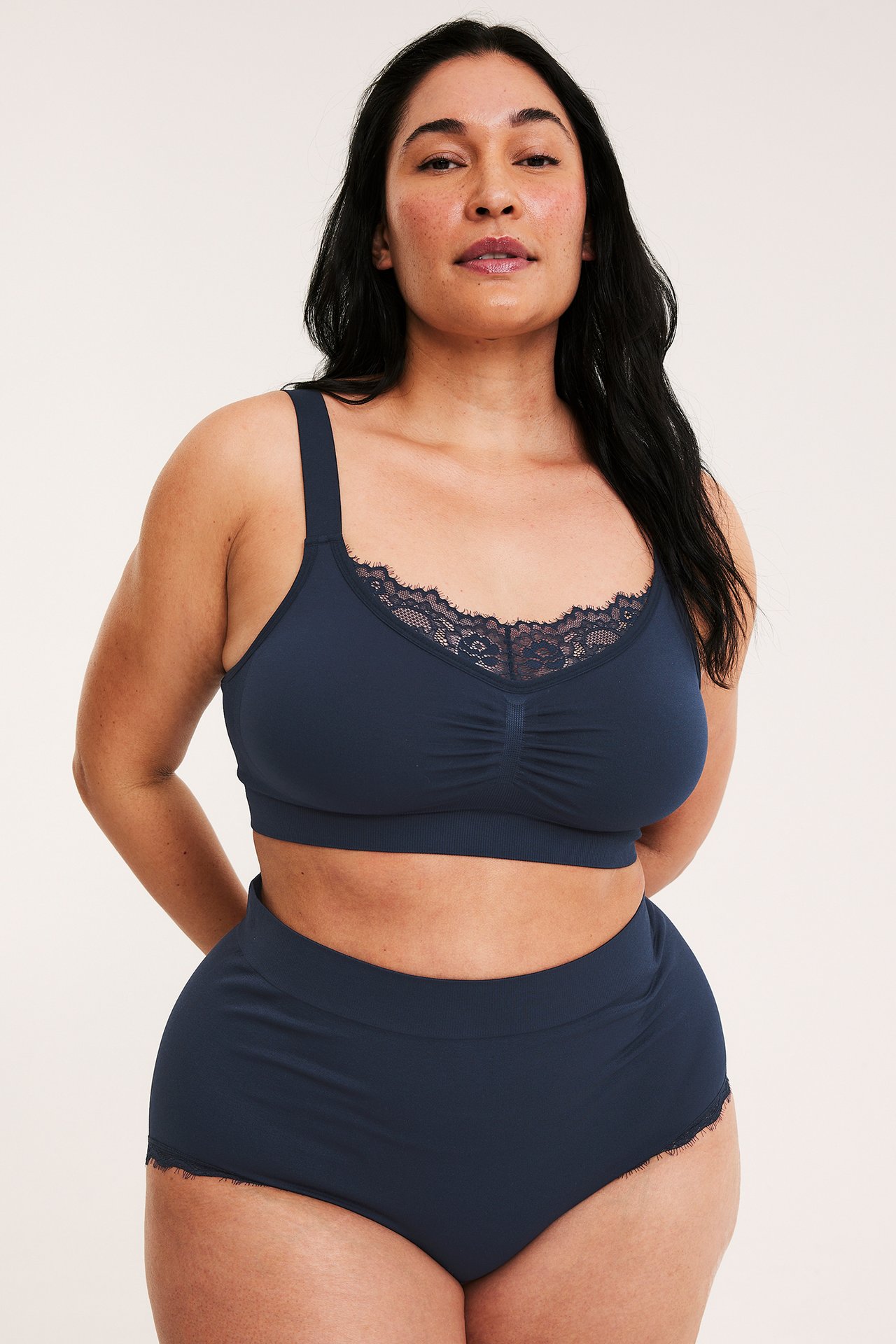Framifrån, kvinna i mörkblå sömlösa högmidjade hipstertrosor med spets och matchande BH.