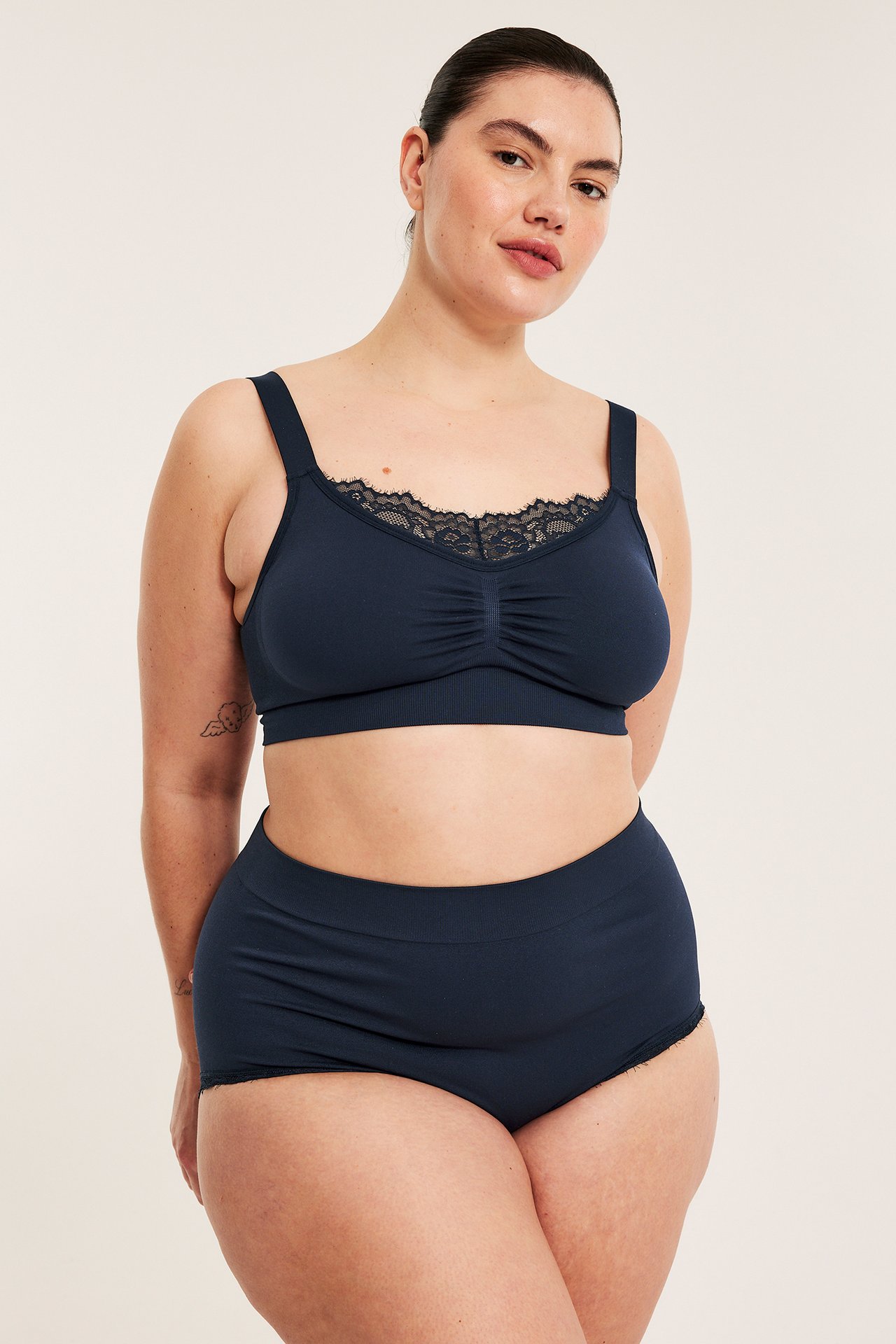 Frontvy av en kvinna i mörkblå sömlösa hipstertrosor och en matchande spetskantad BH.