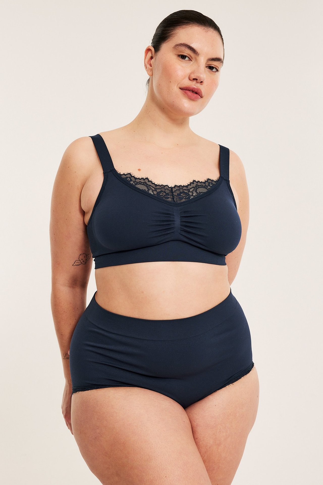 Frontvy av en kvinna i mörkblå sömlösa hipstertrosor och en matchande spetskantad BH.