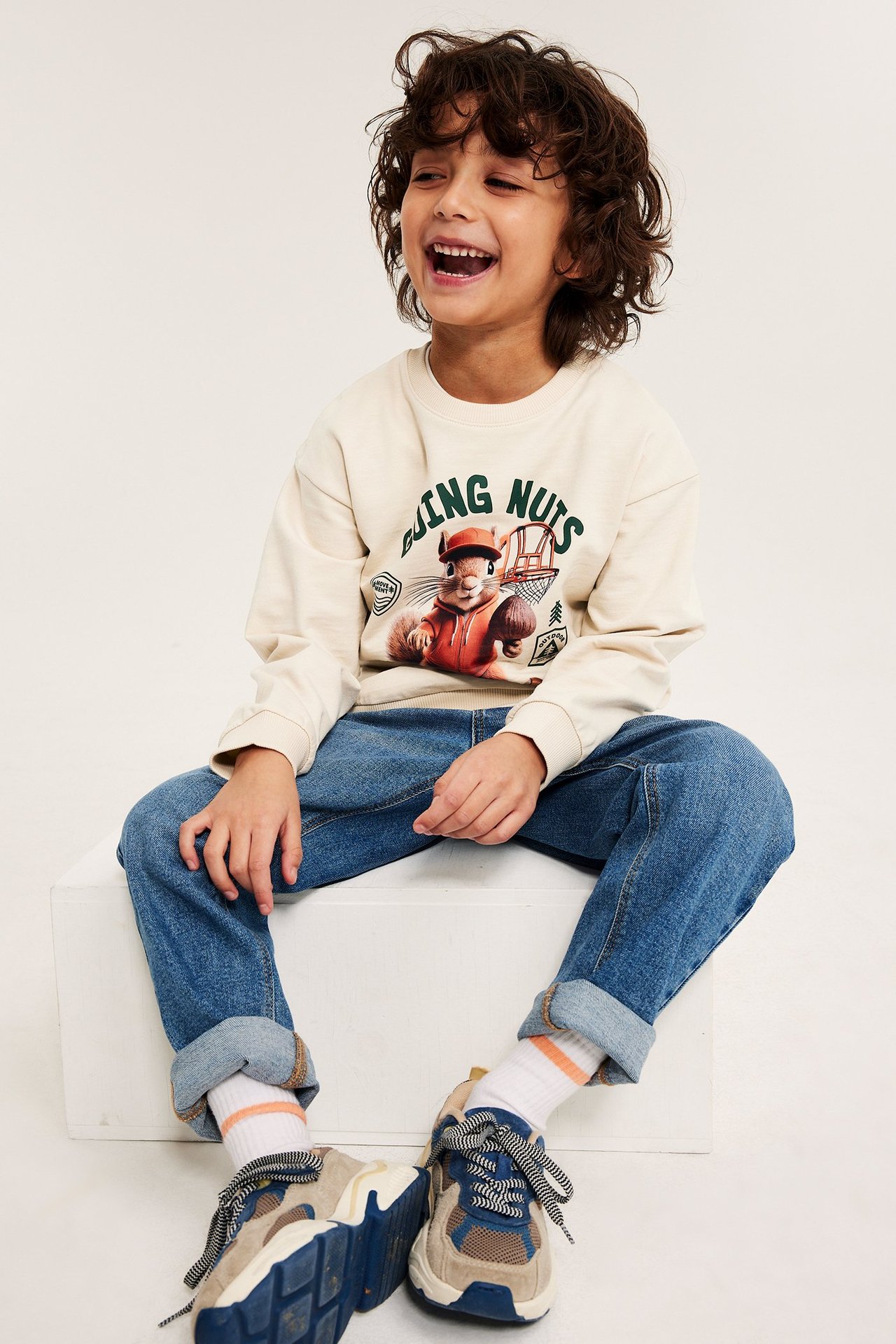 Edestä, poika vaaleanbeigessä puuvillacollegepaidassa oravaprintillä, siniset farkut, tennarit.