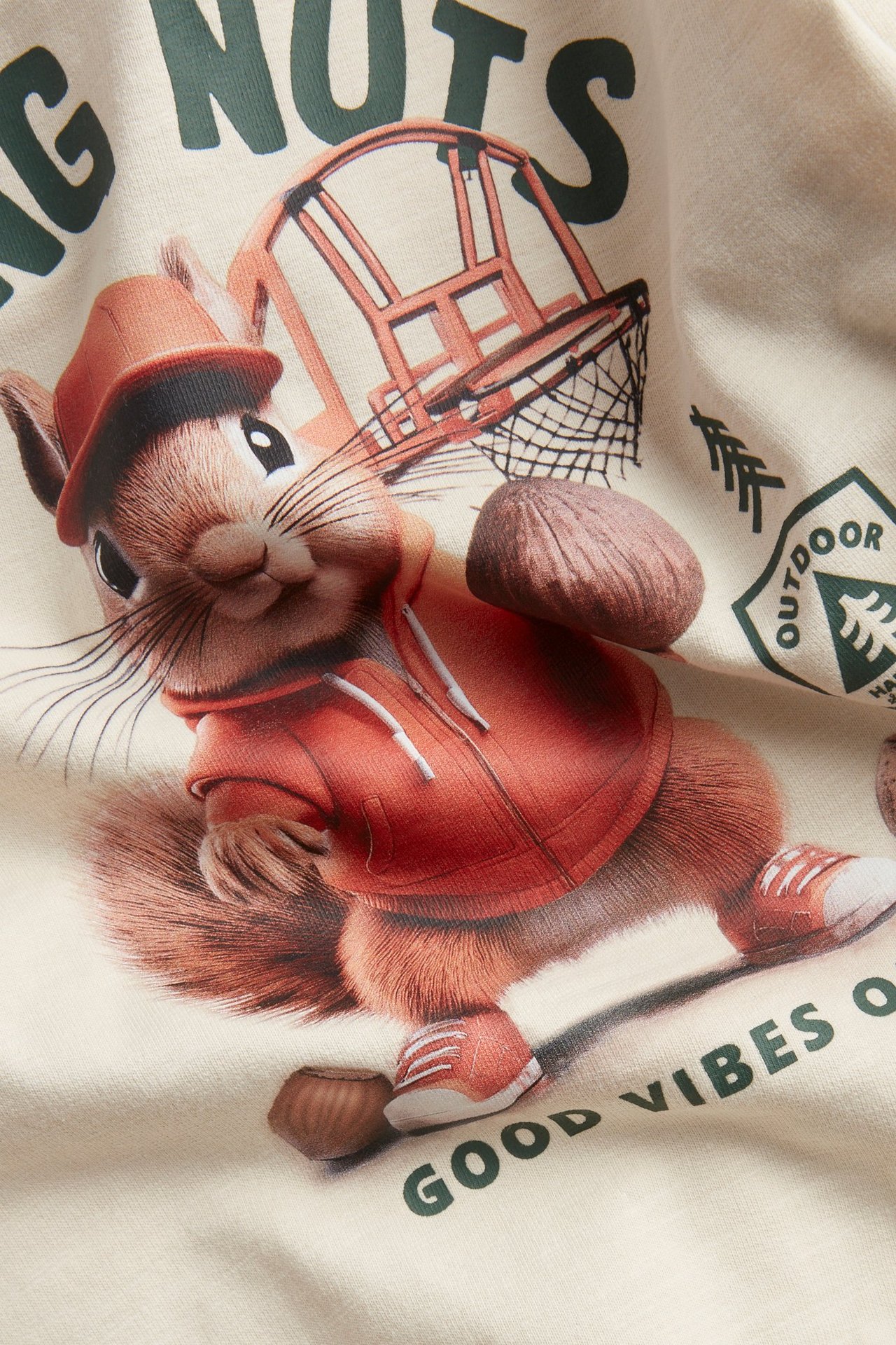 Zbliżenie na miękką, jasnobeżową bluzę bawełnianą z nadrukiem wiewiórki w czerwonej bluzie.