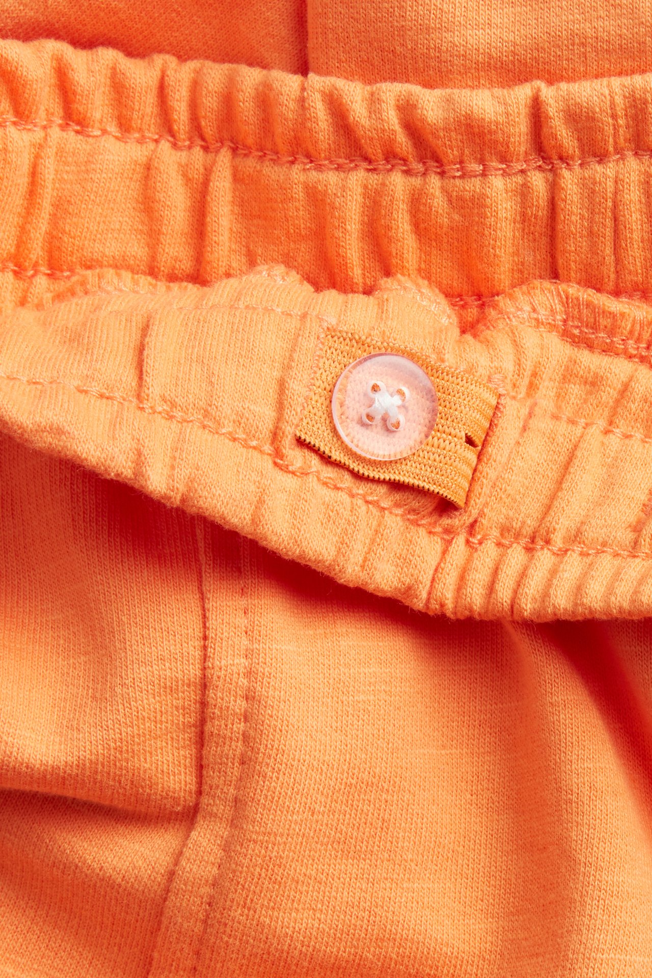Närbild av orange joggingbyxor i bomull med resår i midjan och justerbar knapp.