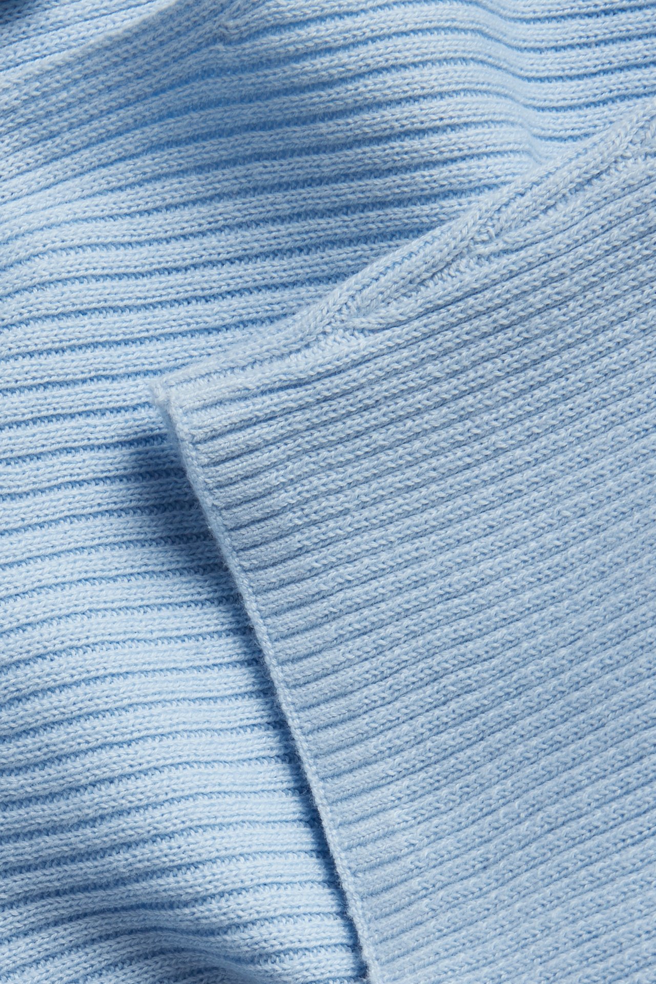 Närbild av en ljusblå ribbstickad bomullströja som visar tygets struktur.