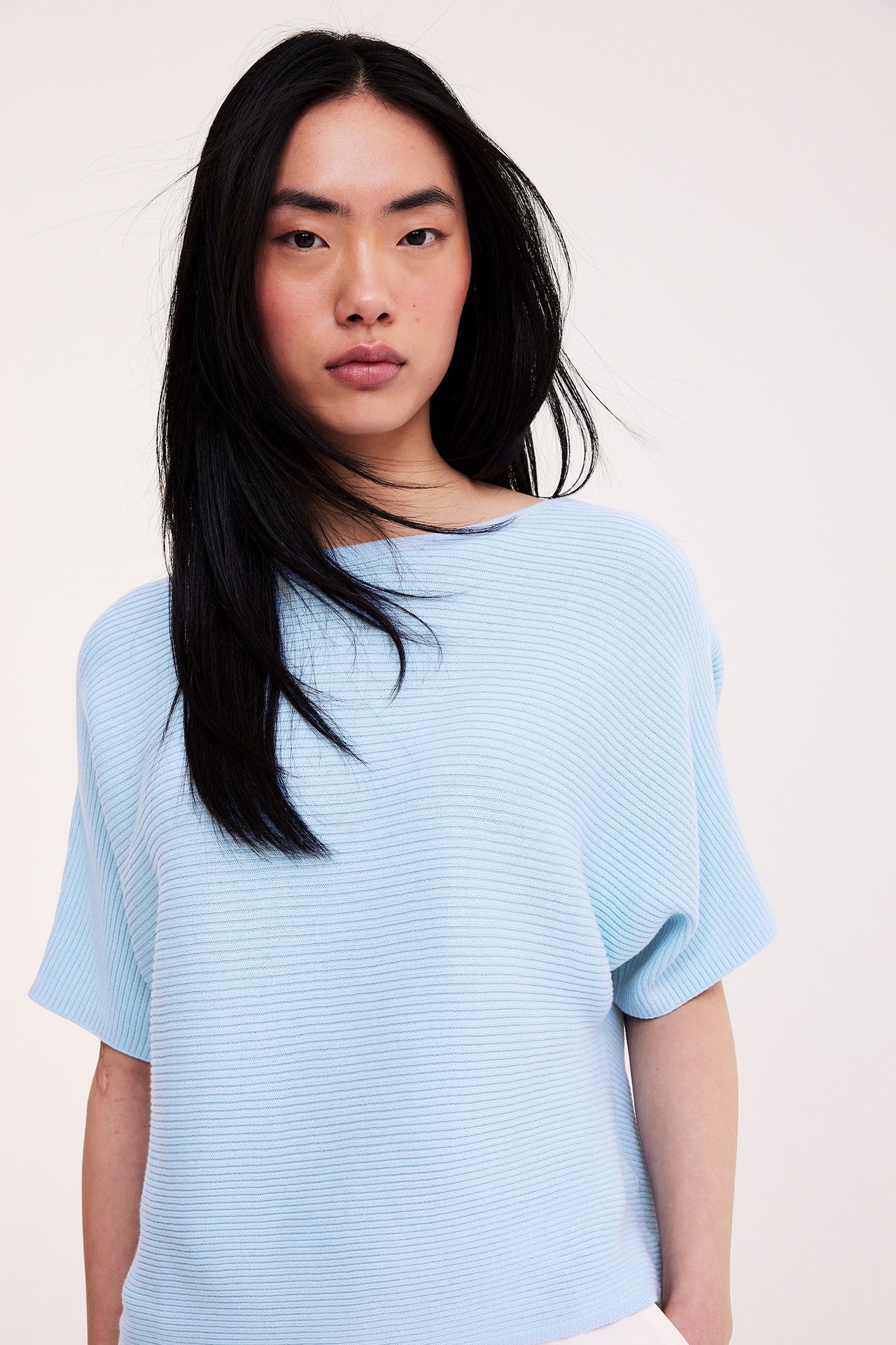 Widok z przodu kobiety w jasnoniebieskim, prążkowanym swetrze bawełnianym z krótkimi rękawami.