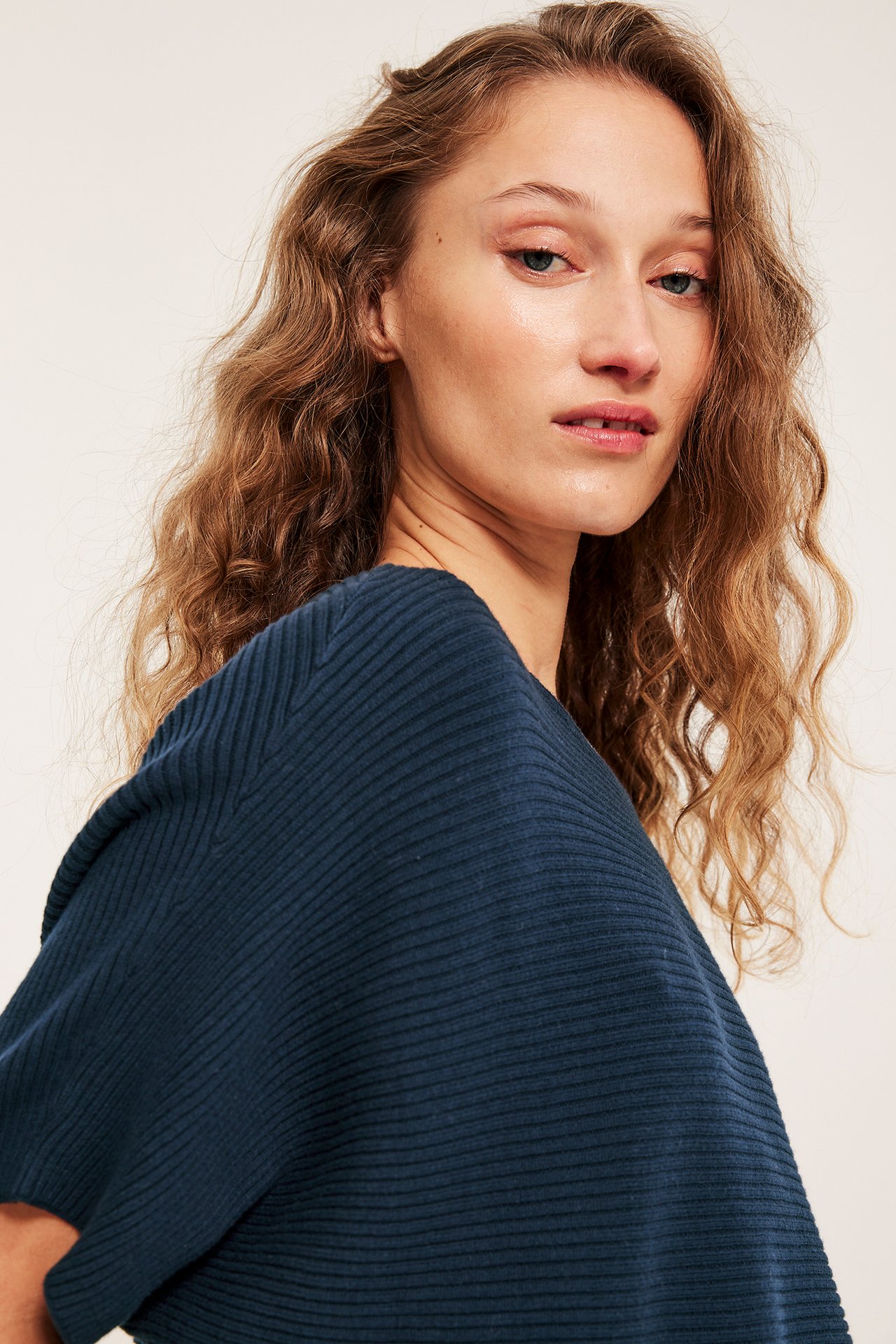 Vinklet nærbilde av en kvinne i en mørkeblå ribbestrikket bomullsgenser.