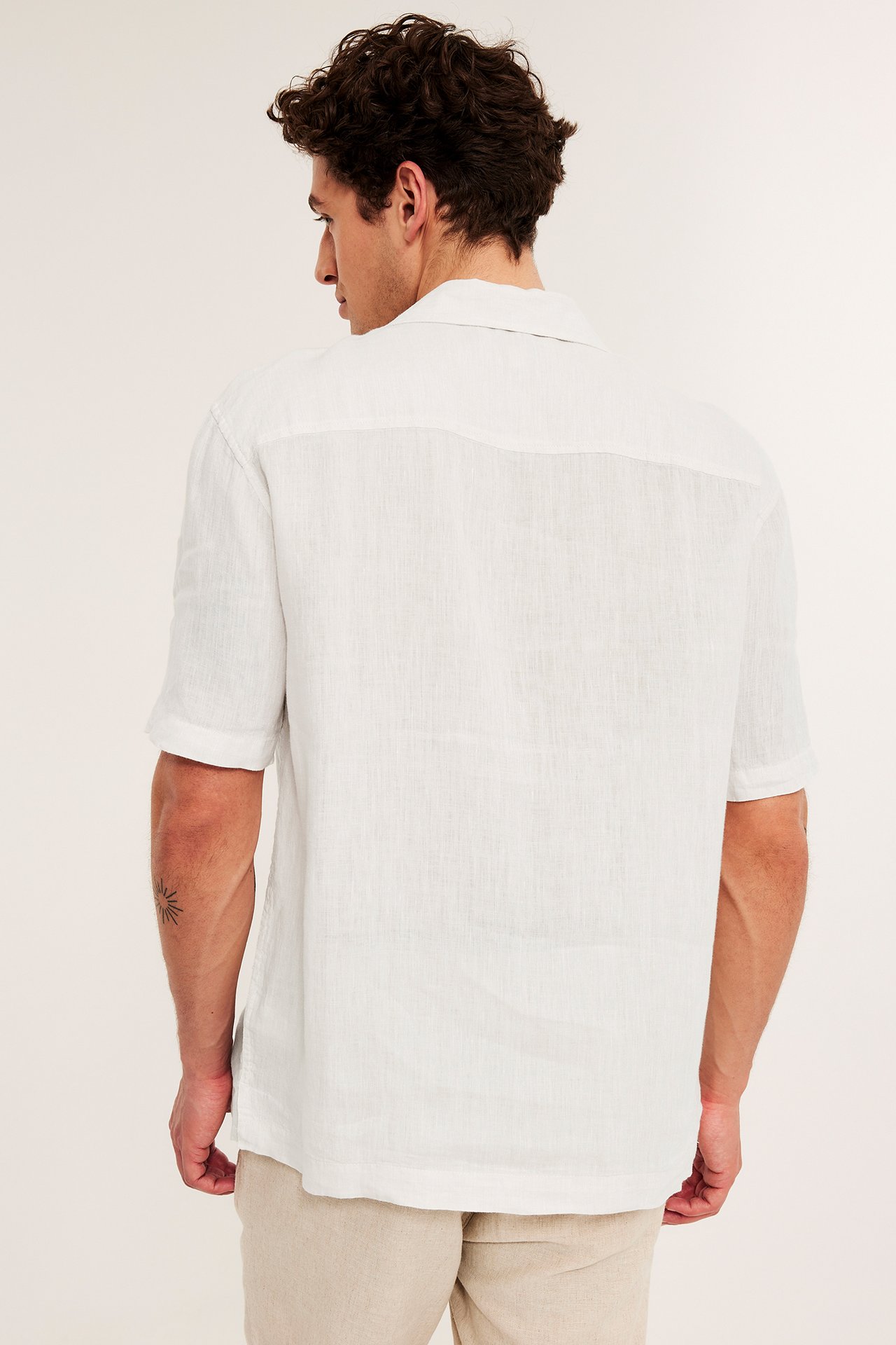 Mies takaapäin, yllään valkoinen meleerattu pellavapaita, lyhythihainen, regular-mitoitus ja vaaleat beiget housut.