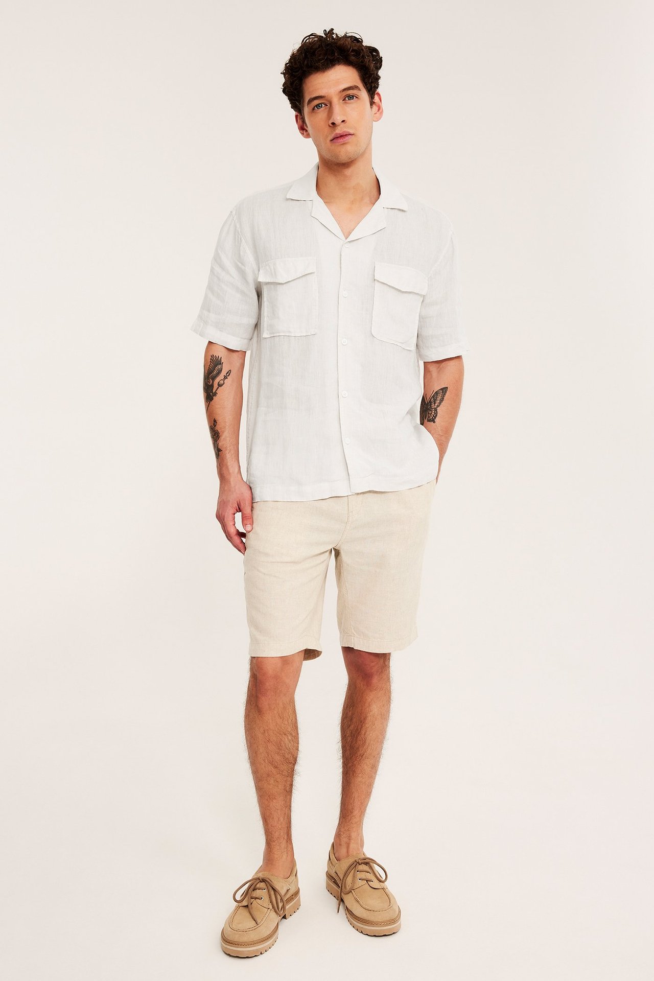 Forfra: mann i hvit melert kortermet linskjorte, beige shorts og snøresko.