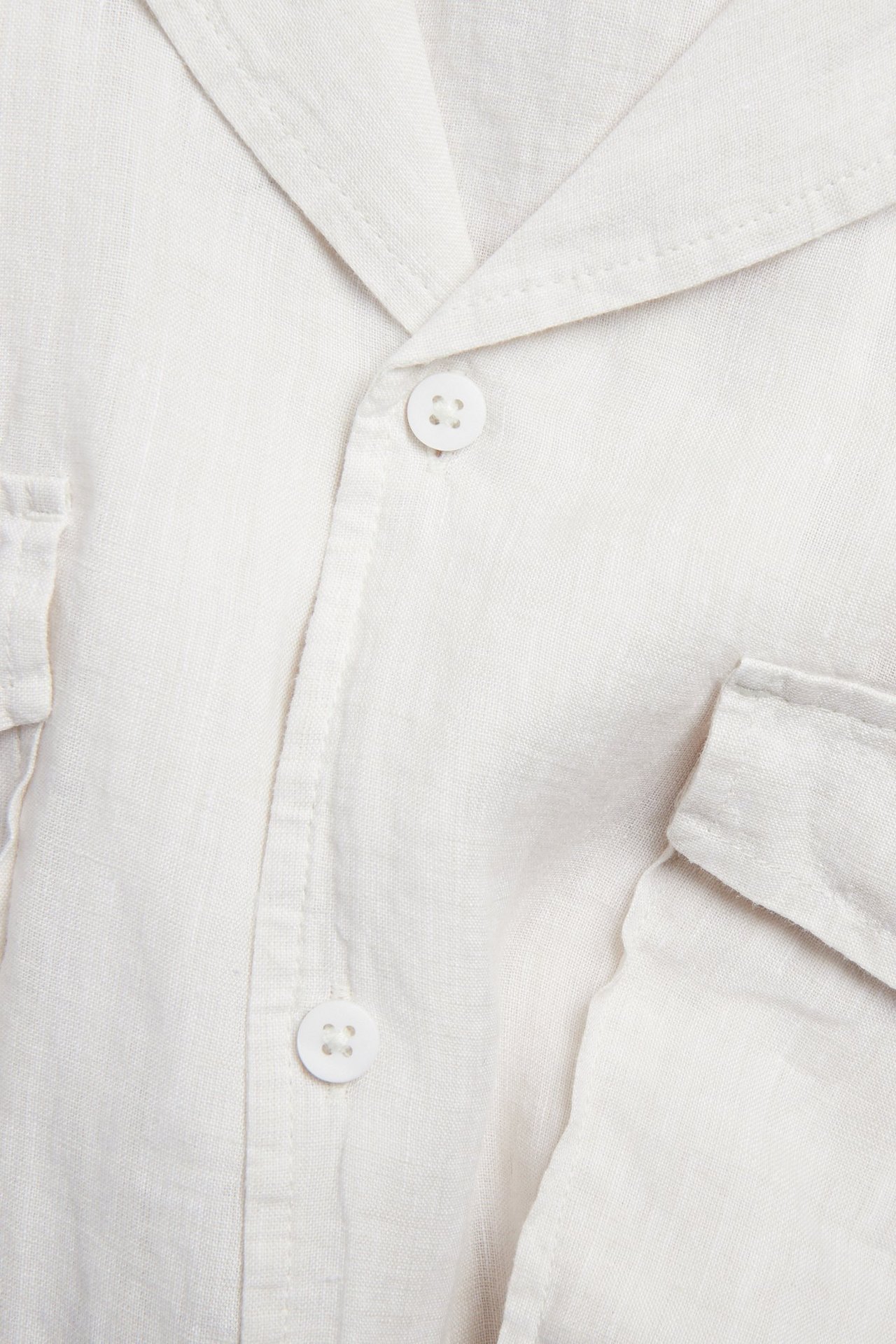 Lähikuva valkoisesta meleeratusta lyhythihaisesta pellavapaidasta, jossa on resort-kaulus, napitus ja rintataskut.