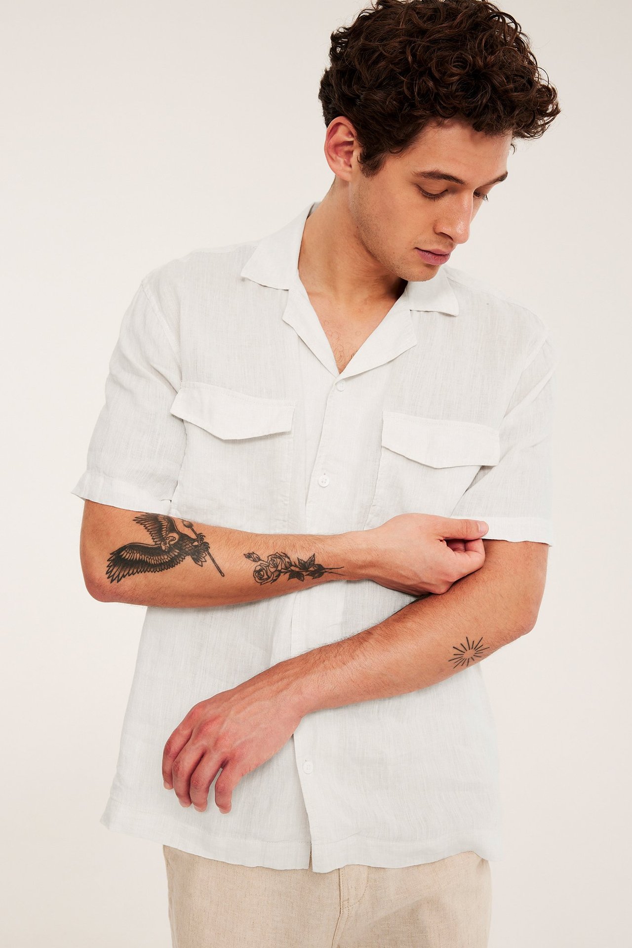 Framifrån: Man i vit melerad kortärmad linneskjorta med resortkrage, bröstfickor och beiga byxor.