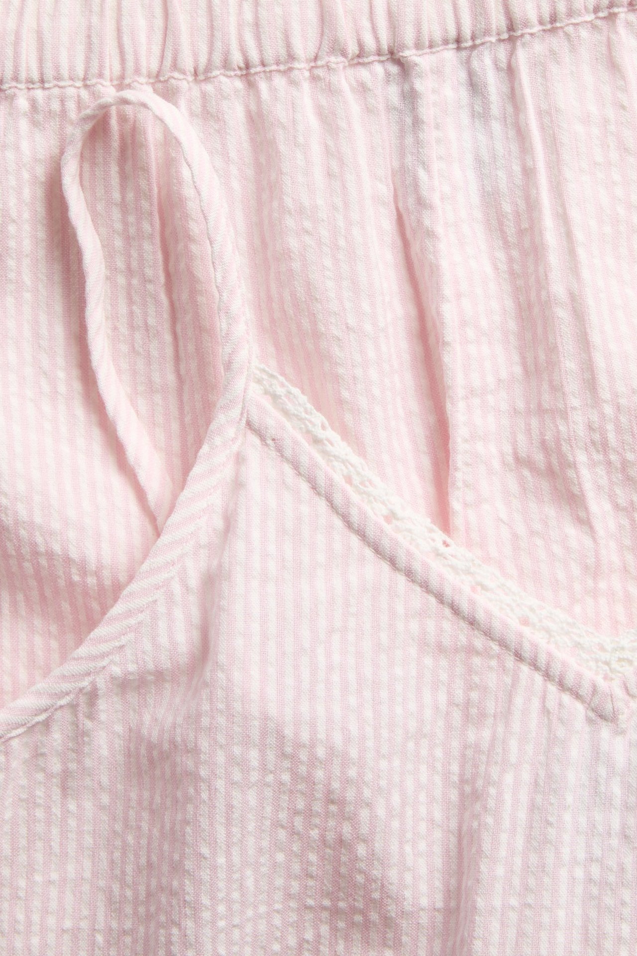 Lähikuva vaaleanpunaisesta ja valkoraidallisesta puuvillapyjamasetistä, topissa pitsireuna, shortseissa kiristysnyöri.