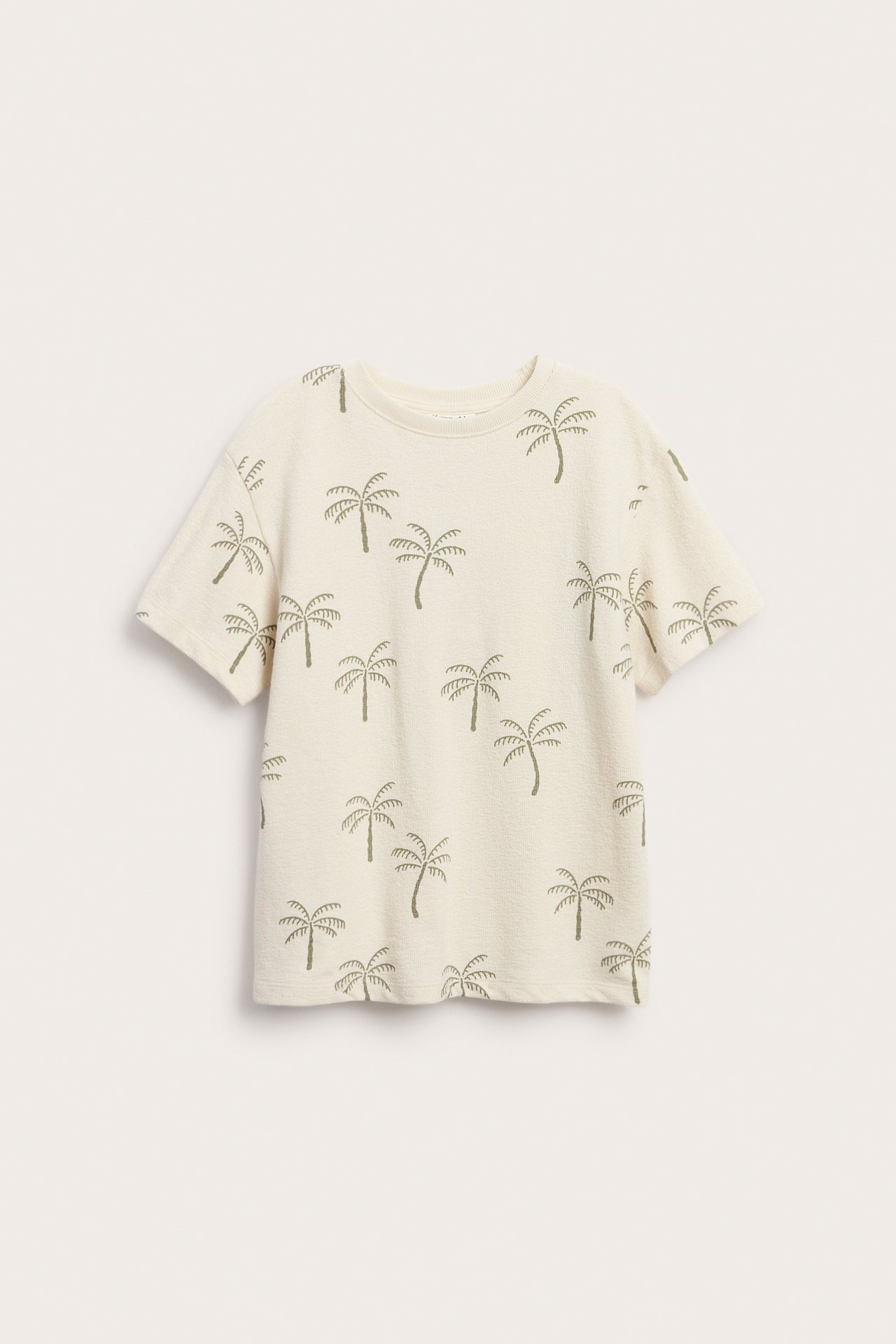 Widok z przodu beżowej koszulki bawełnianej z krepy o luźnym kroju z zielonym wzorem w palmy.