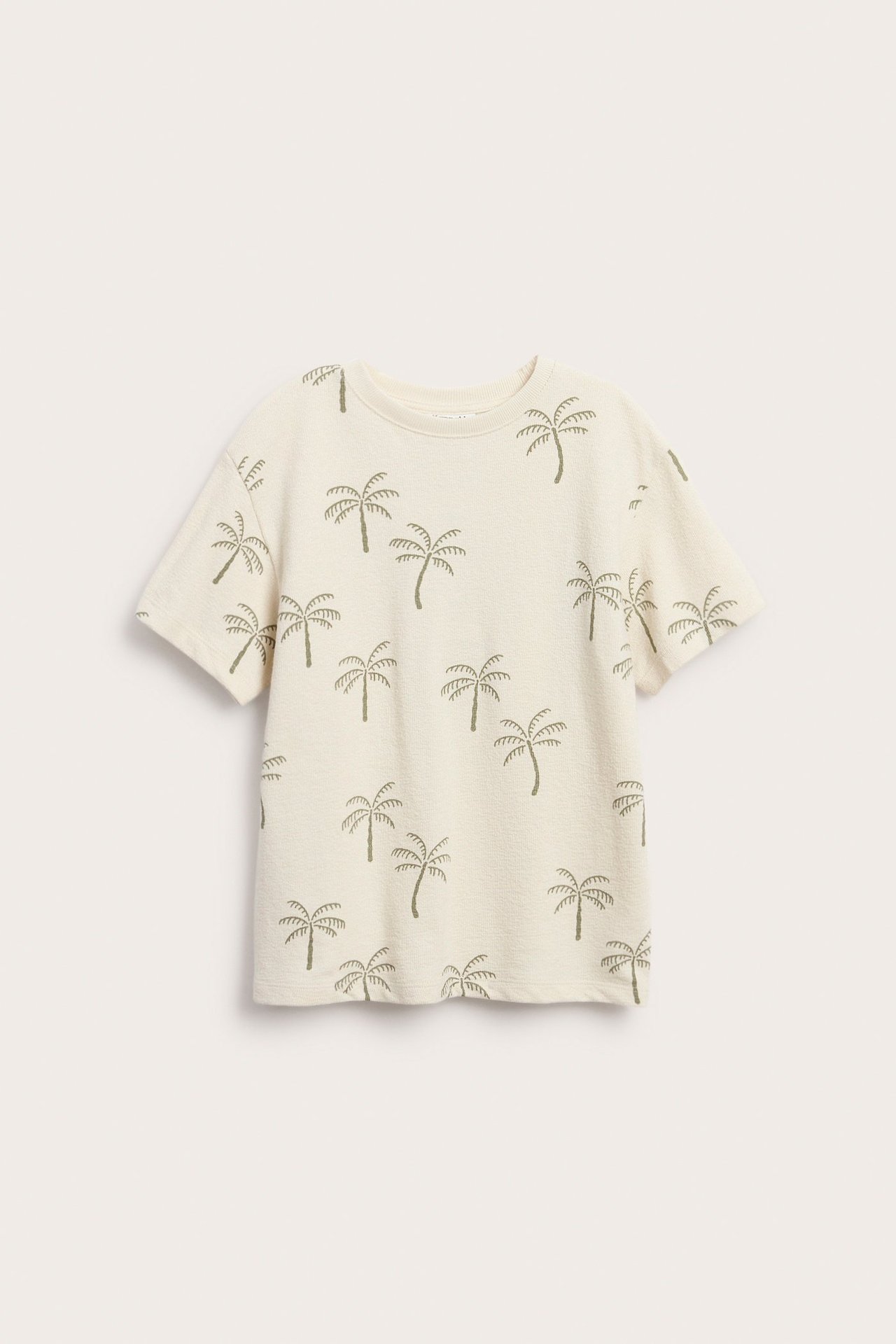 Widok z przodu beżowej koszulki bawełnianej z krepy o luźnym kroju z zielonym wzorem w palmy.